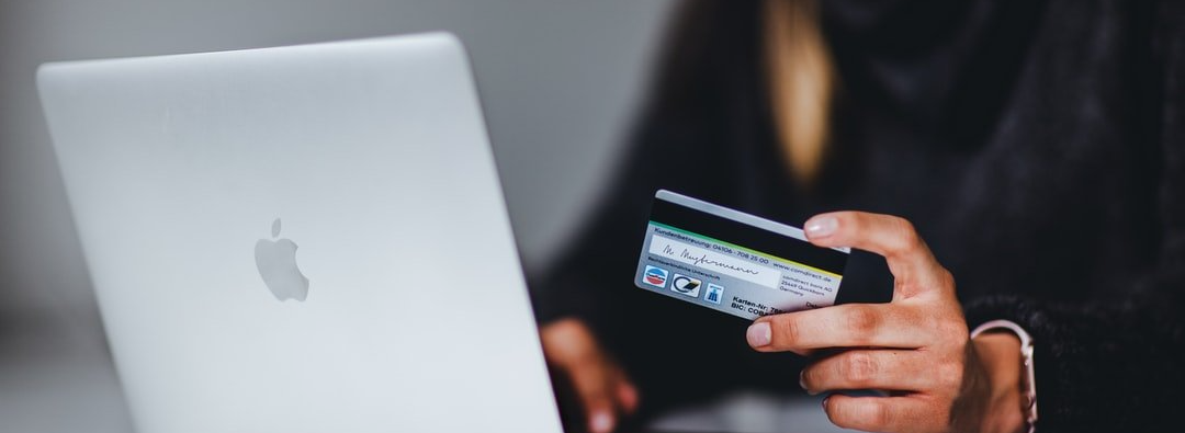 A person is holding a credit card in front of a laptop computer.