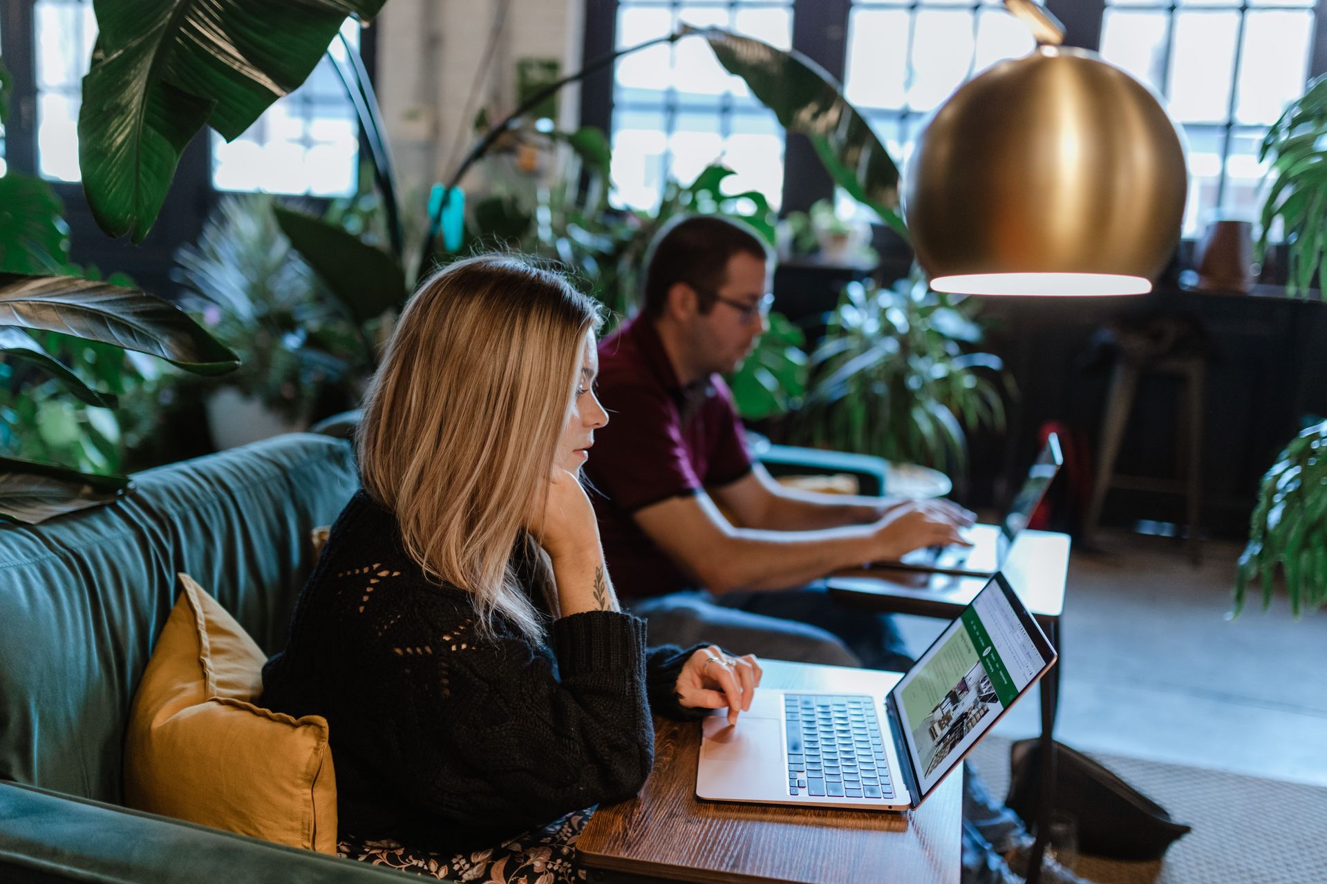A man and a woman are sitting on a couch using laptops.