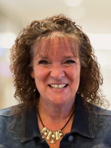 A woman wearing a necklace and a denim jacket is smiling for the camera.