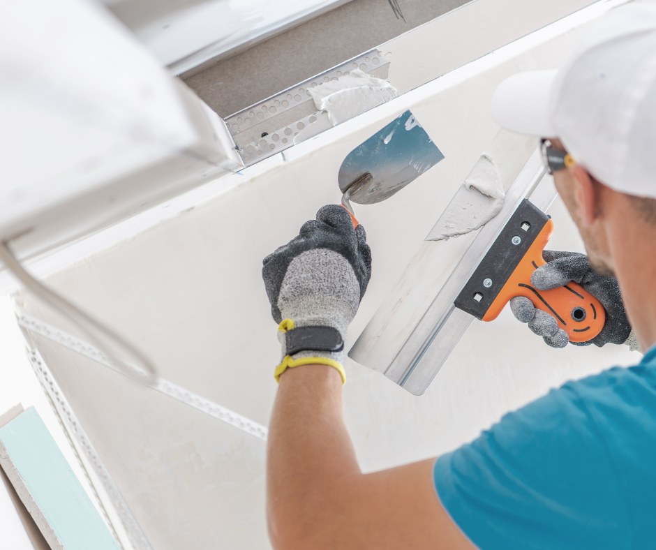 Worker sanding a white wall with a power sander and putty knife during repairs