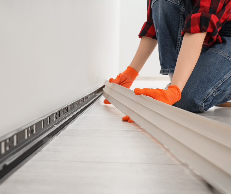 Worker in orange gloves installing white flooring boards on a room floor