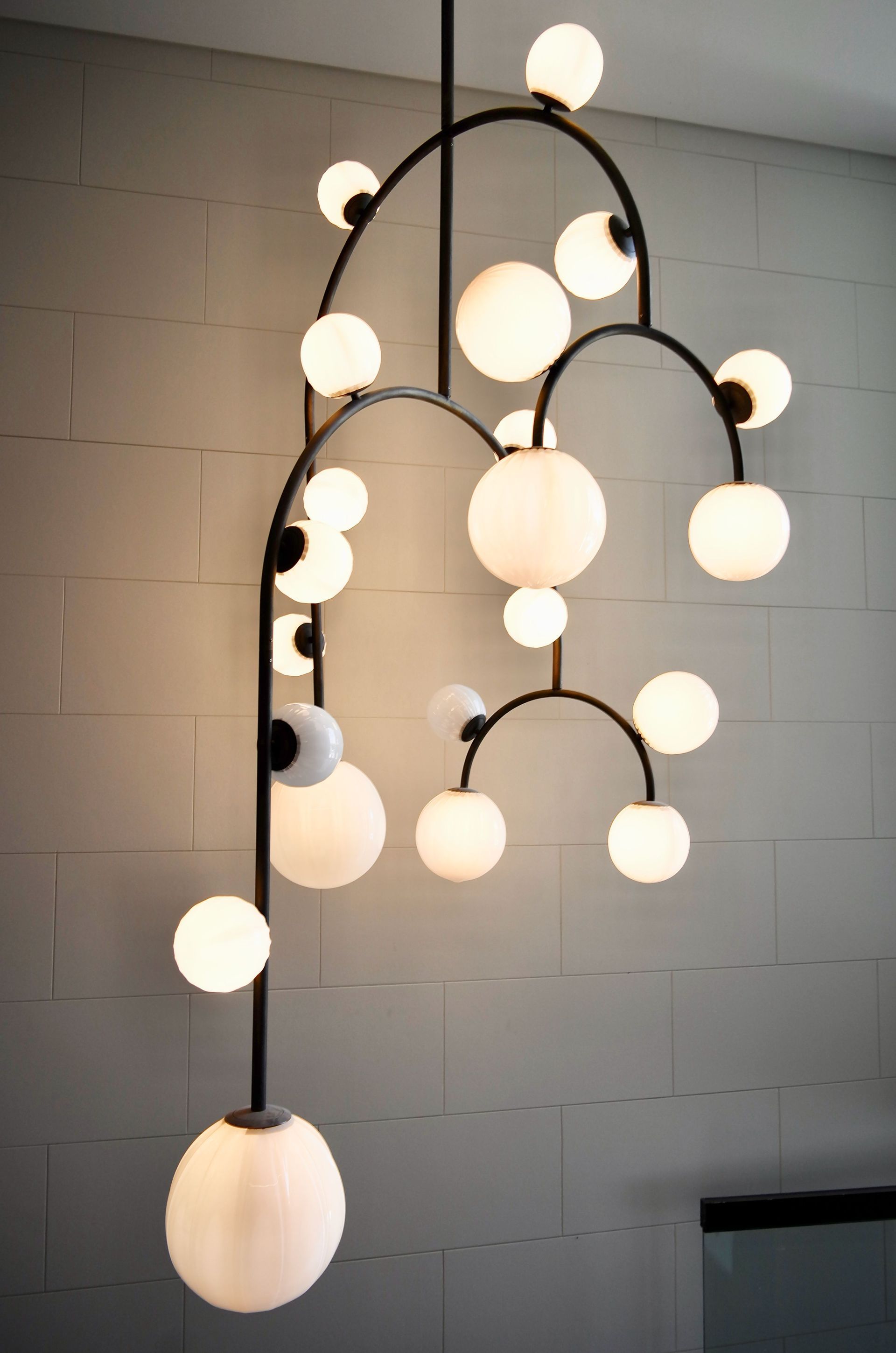 Modern pendant chandelier with glowing white globes on black curved branches against a gray wall