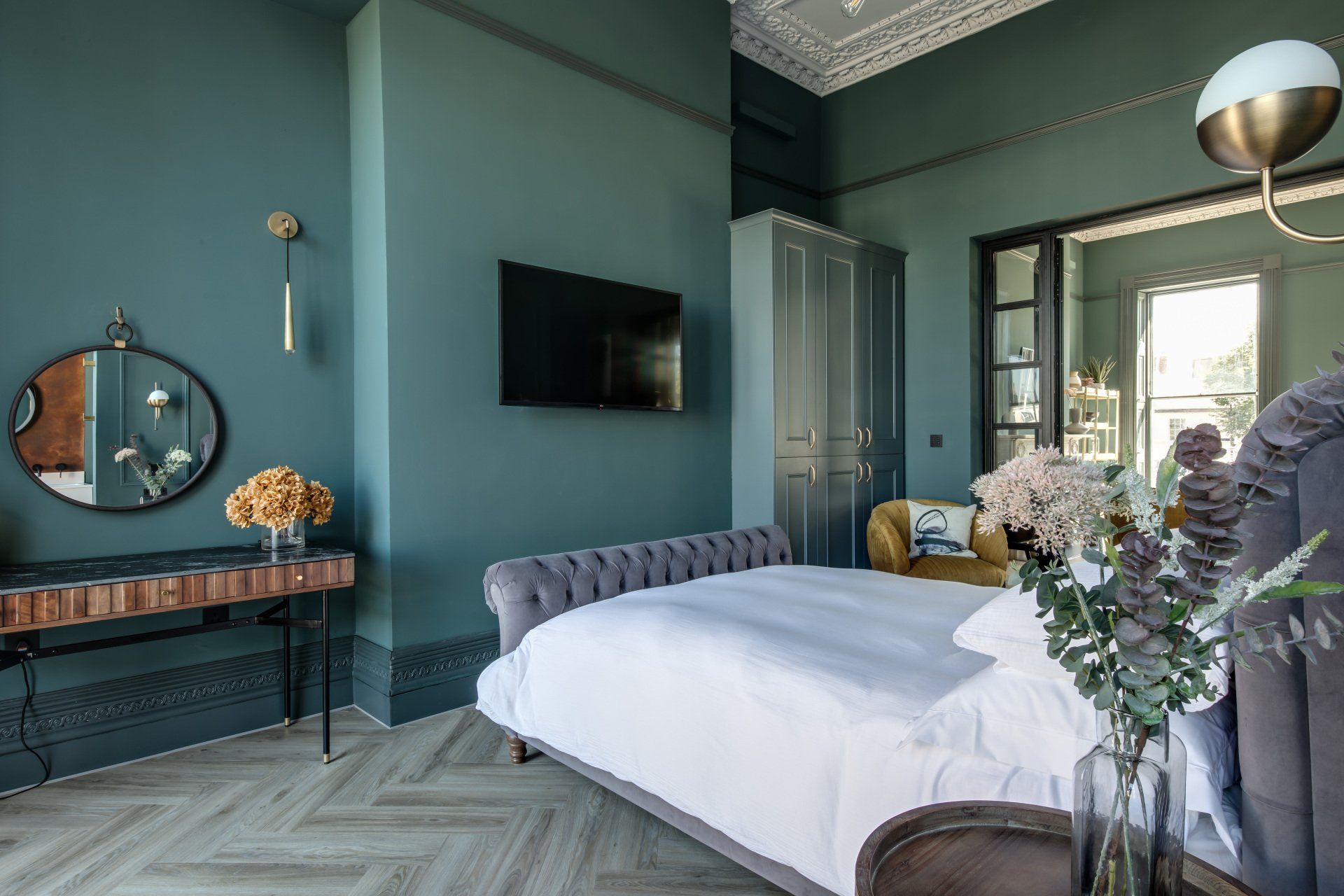 A bedroom with a bed , television , mirror and bench.