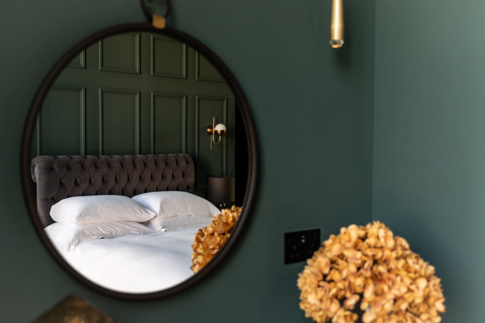 A bedroom with a round mirror hanging on the wall.