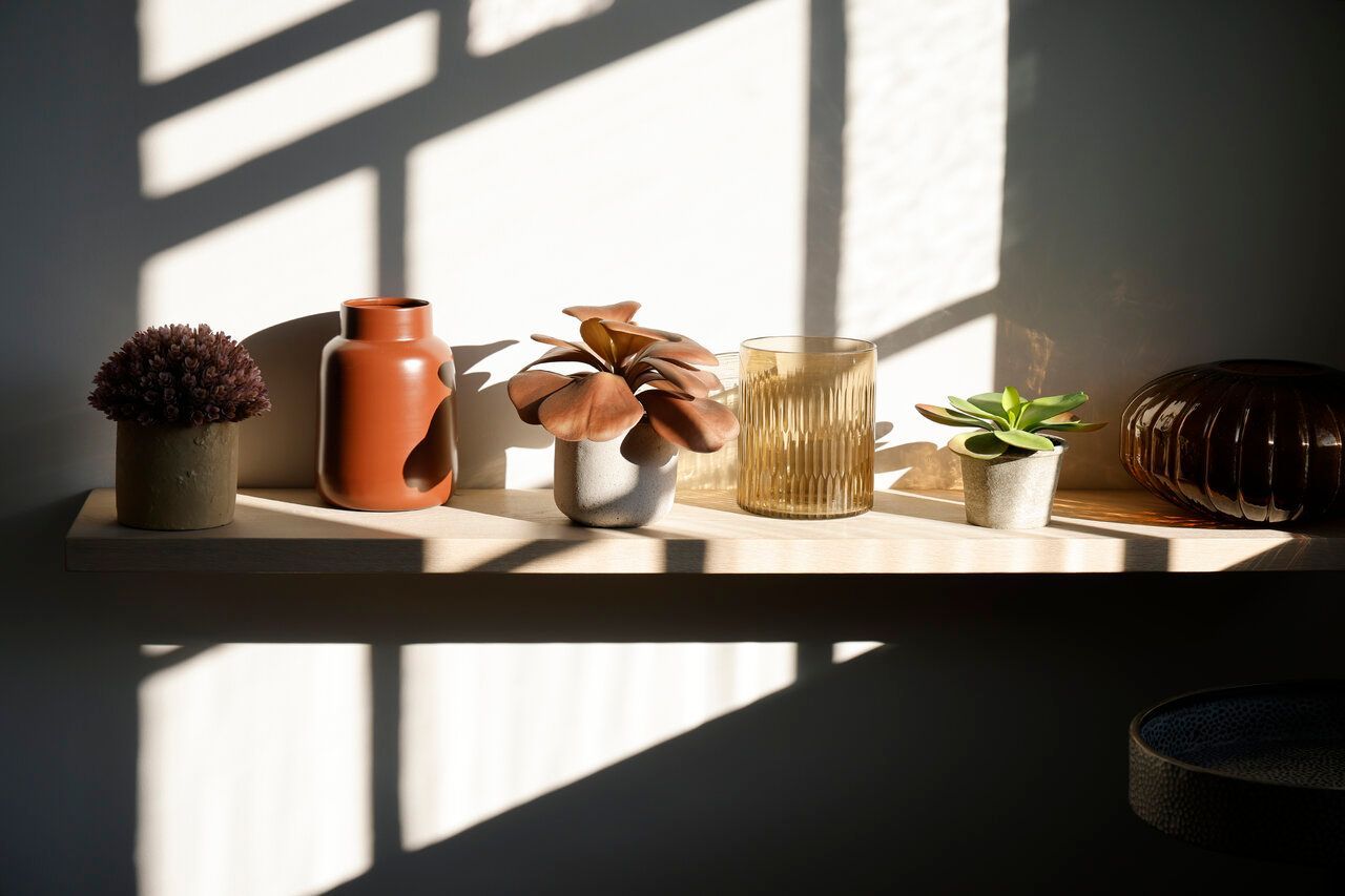 A shelf with vases and plants on it in front of a window.