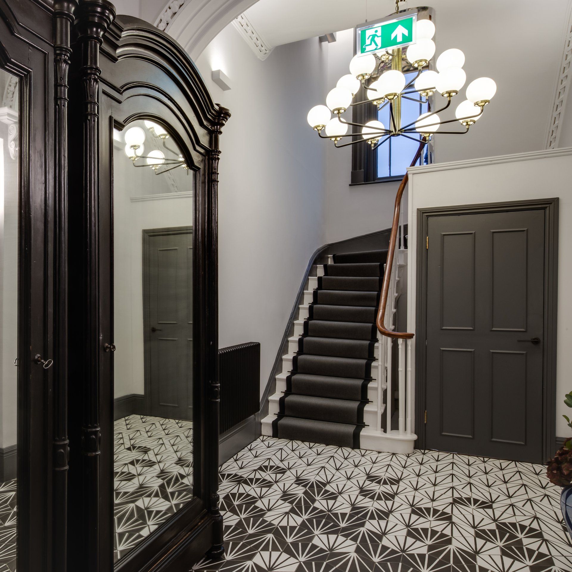 A hallway with a staircase and a green exit sign
