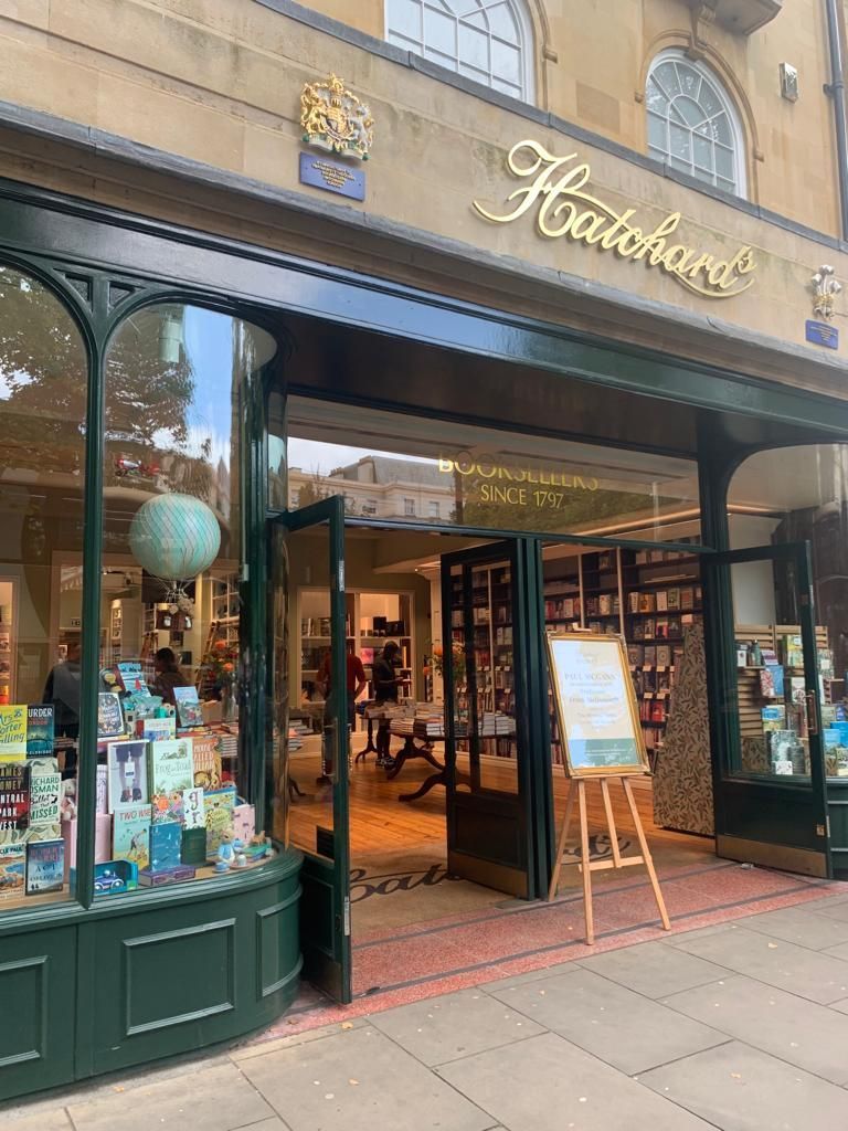 A bookstore with a green building and a wooden easel in front of it.