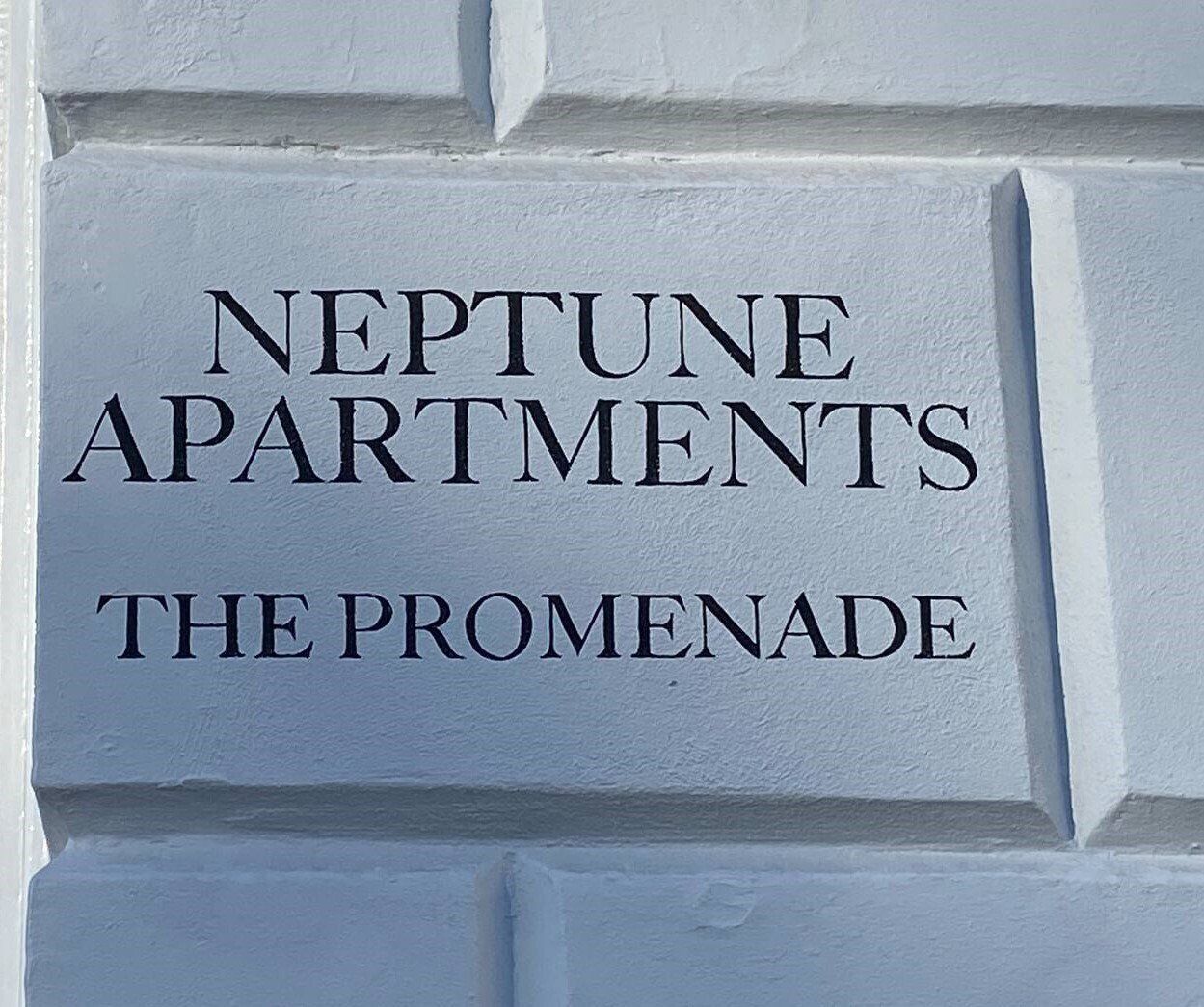 A sign on a wall that says neptune apartments the promenade