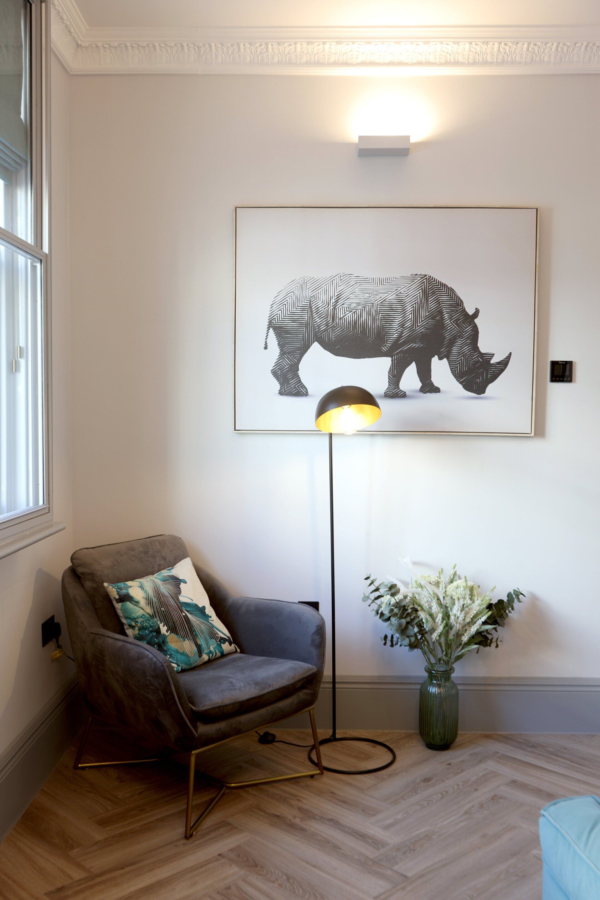 A living room of a luxury serviced apartment with a chair a lamp and a painting of a rhino on the wall