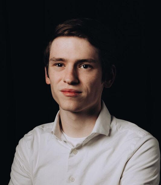 Portrait of a person in a white shirt against a dark background, looking at the camera with a slight smile