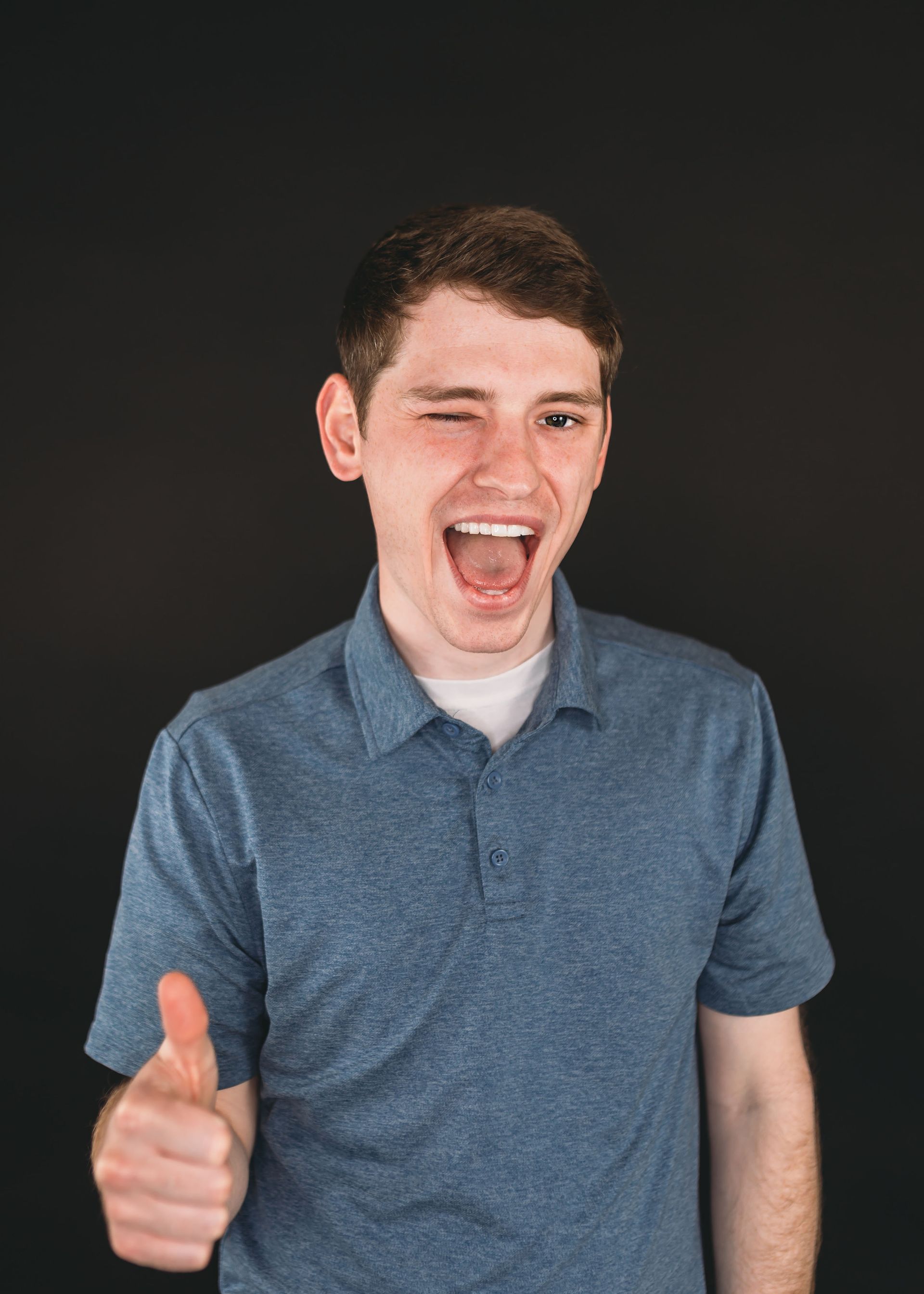 Smiling person in a blue polo shirt giving a thumbs-up against a dark background