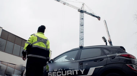 A security guard is standing next to a security car.