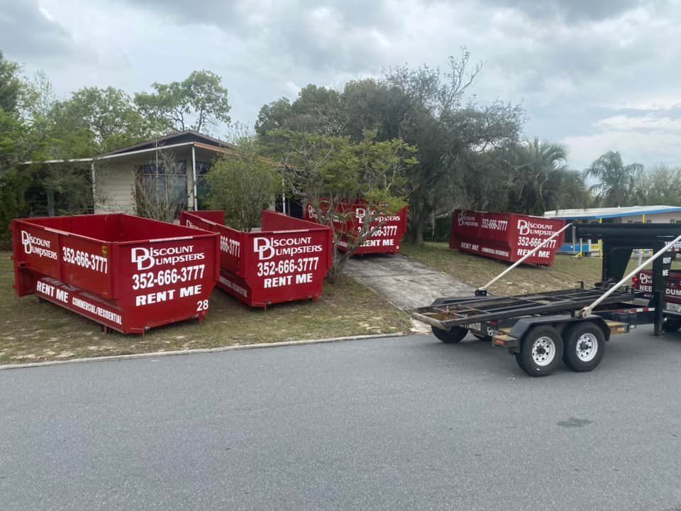 A dumpster is sitting on the side of the road next to a trailer.