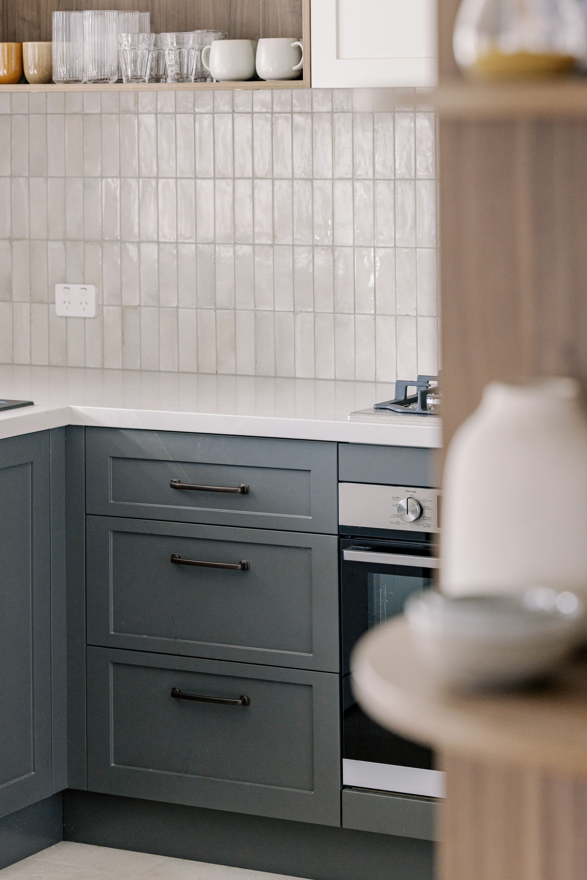 Gray kitchen cabinets with a white countertop and tile backsplash.