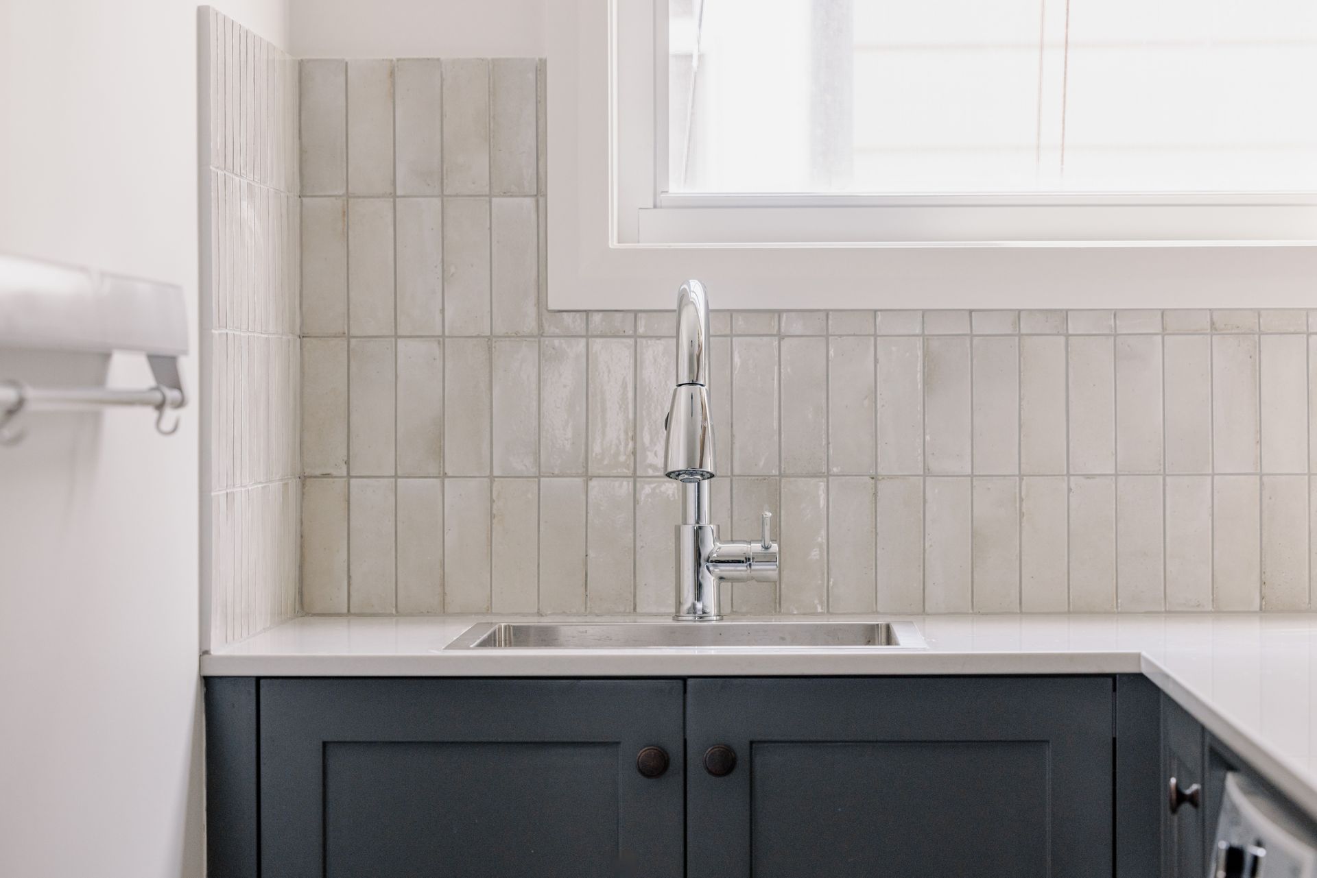 Sink with backsplash, faucet, and dark blue cabinets under a window.