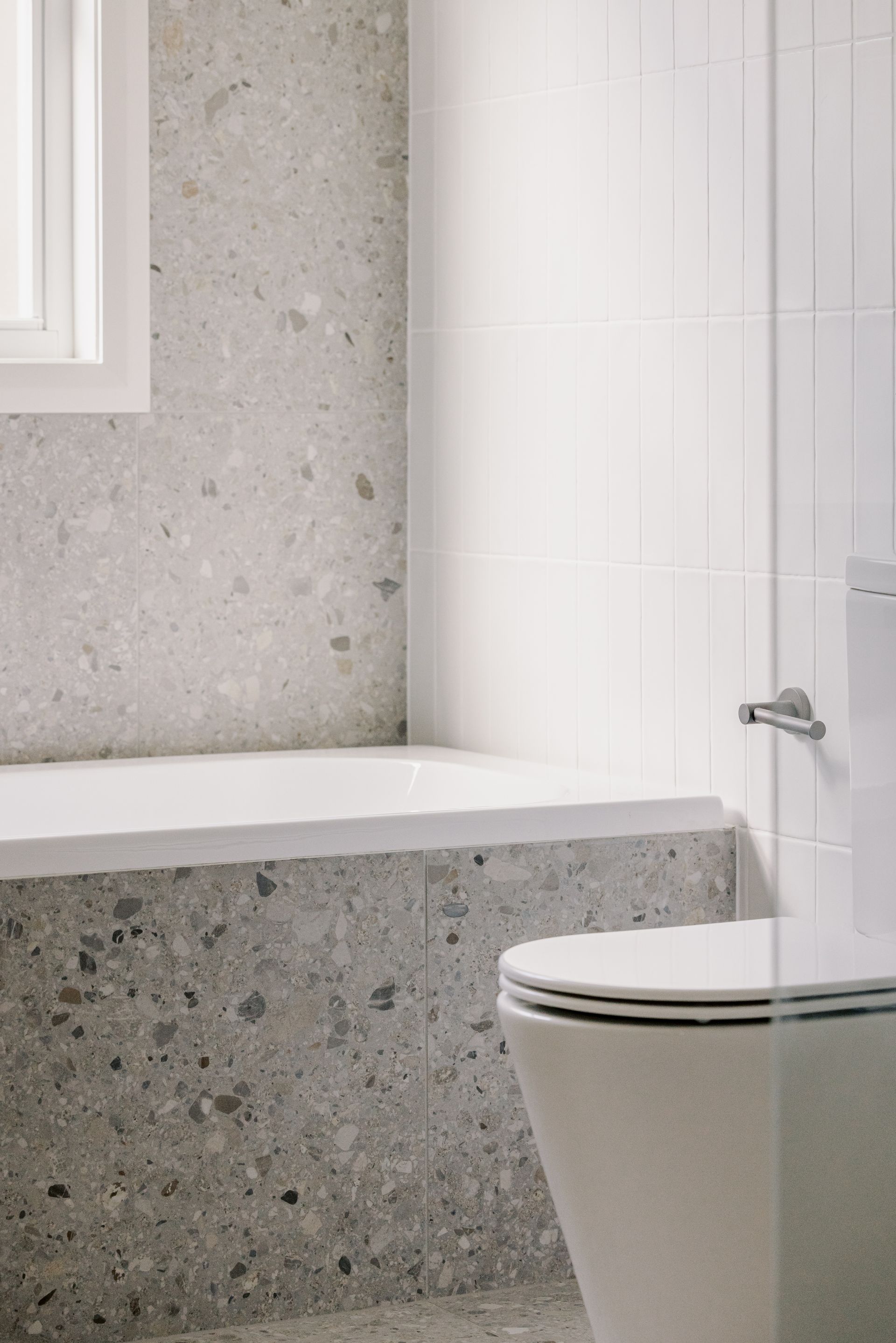 Bathroom with terrazzo-like walls and a white toilet. A window is visible.