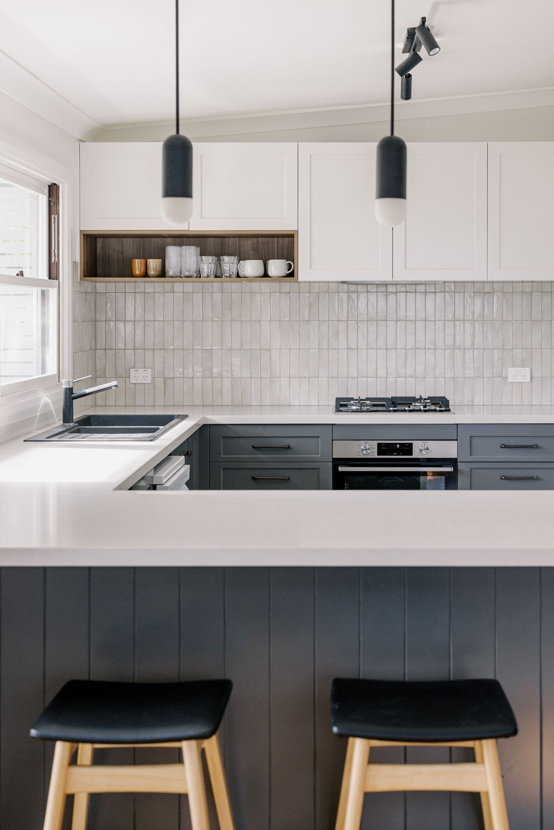 Modern kitchen with white countertops, gray cabinets, and wooden bar stools.