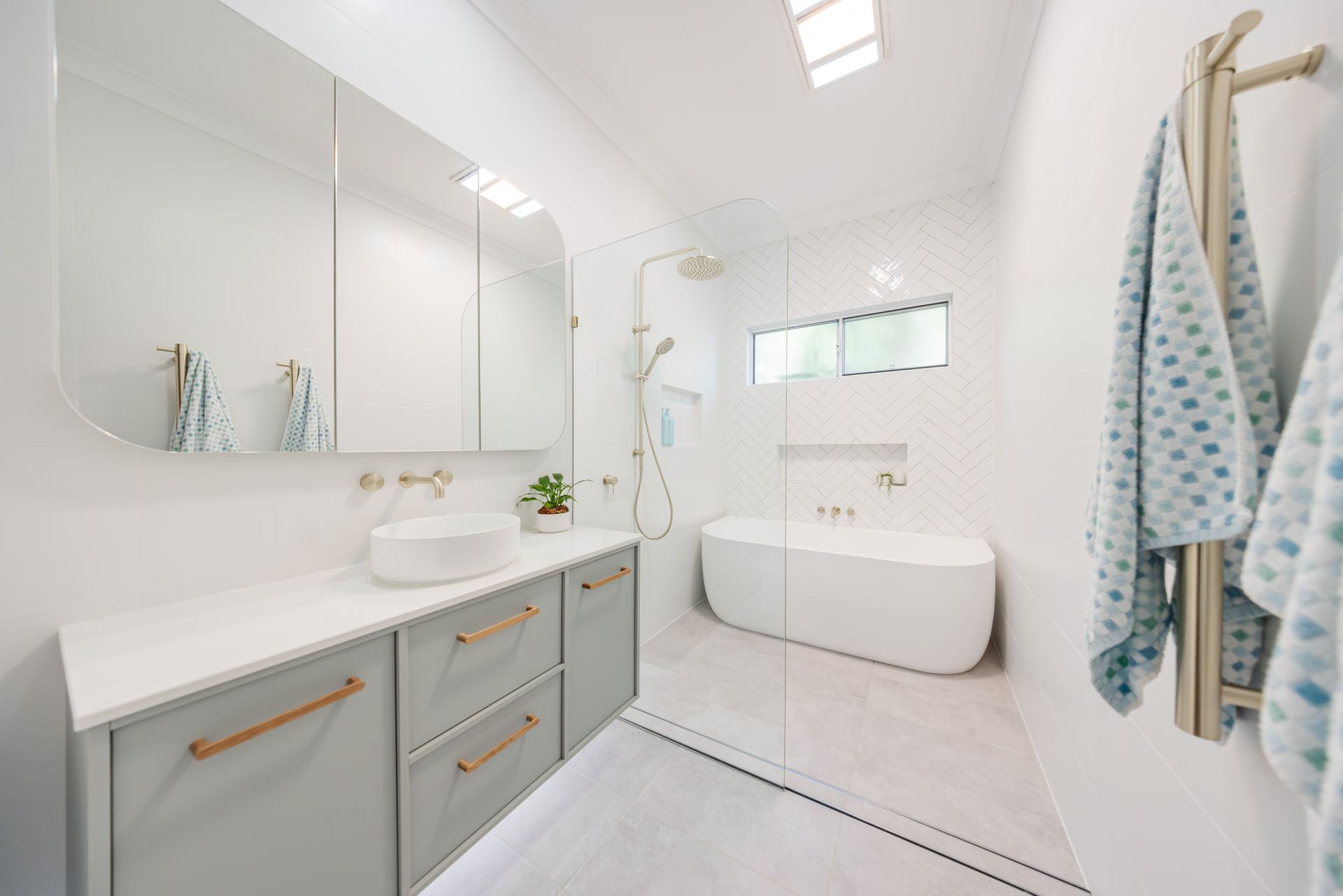 Modern, white bathroom with gray vanity, round sink, tub, and gold accents.