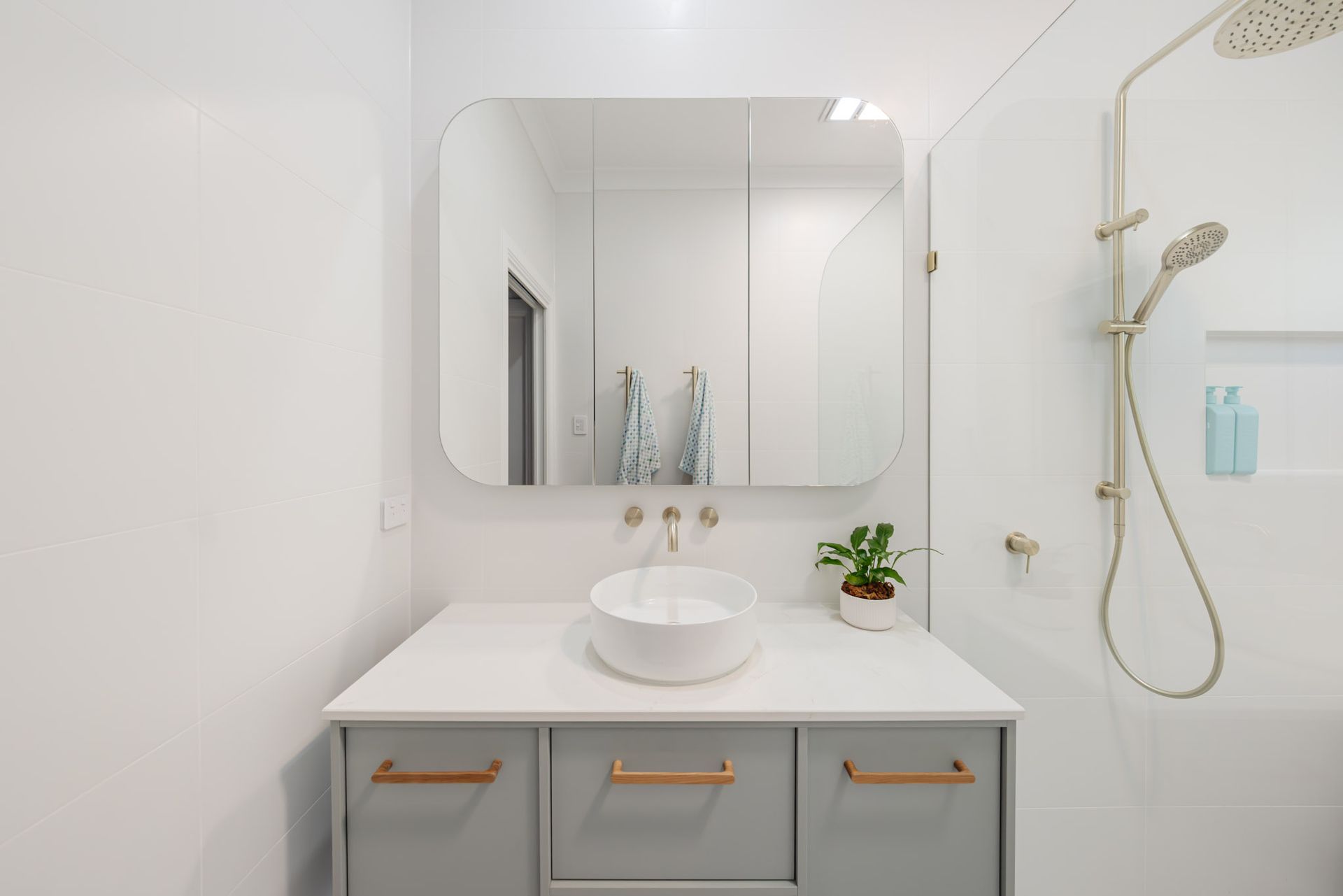 Bathroom with gray vanity, white countertop, round sink, large mirror, and gold fixtures.