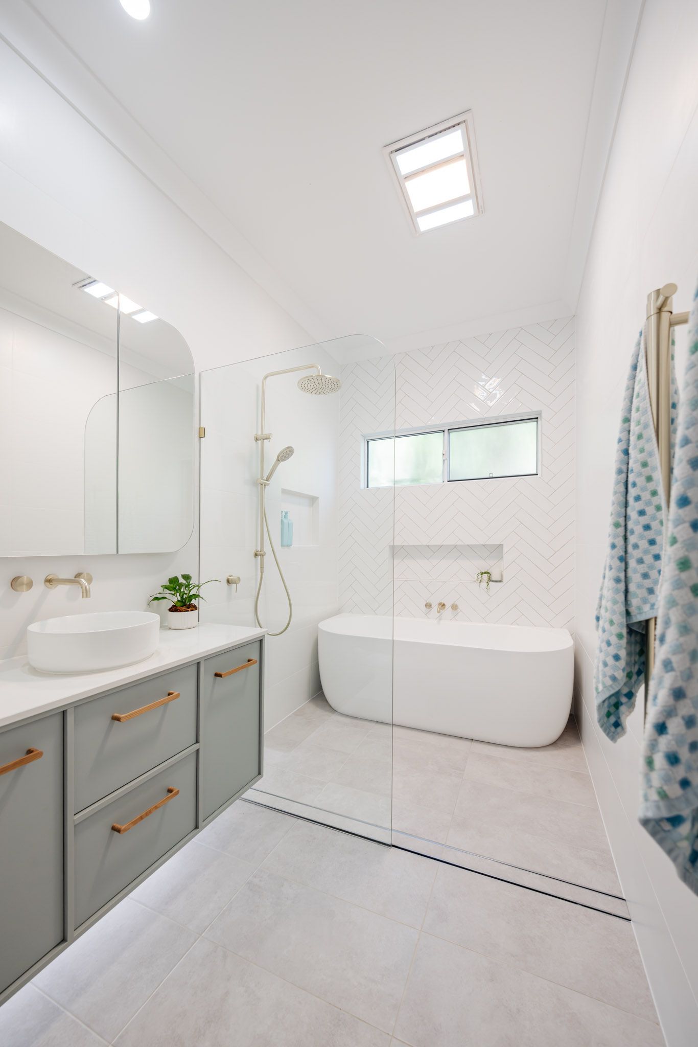 Modern white bathroom with a freestanding tub, gray vanity, and patterned tile accent wall.