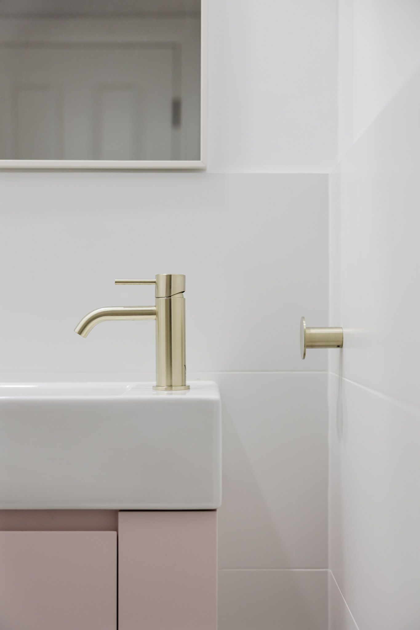 Modern bathroom with white walls, pink cabinet, gold faucet, and matching towel holder.