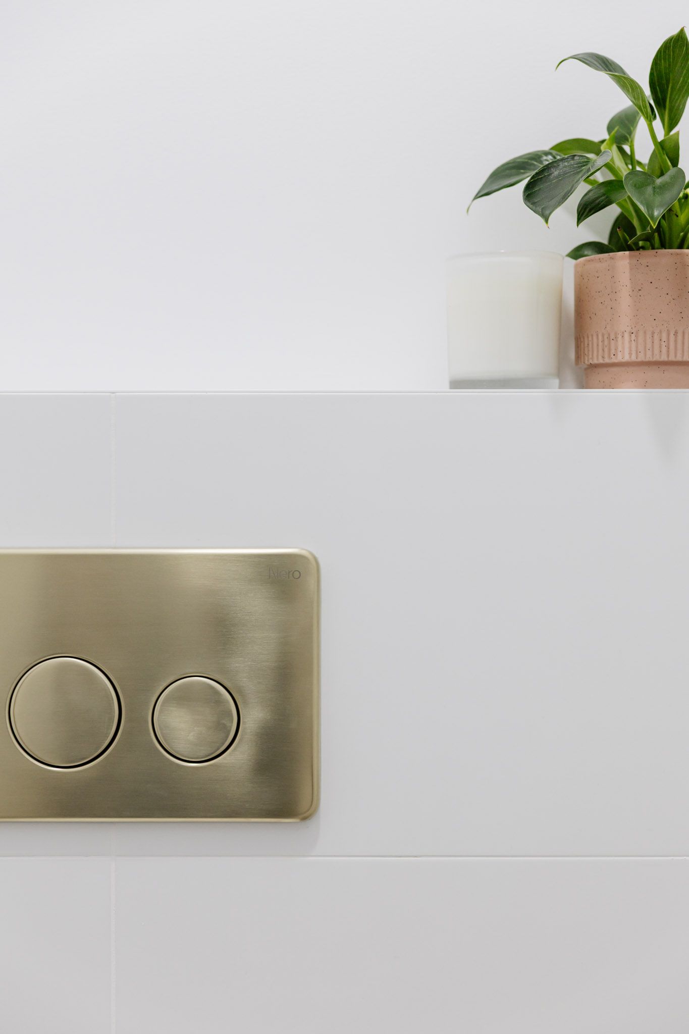 Brass flush plate on white tile wall, small plant and candle on shelf.