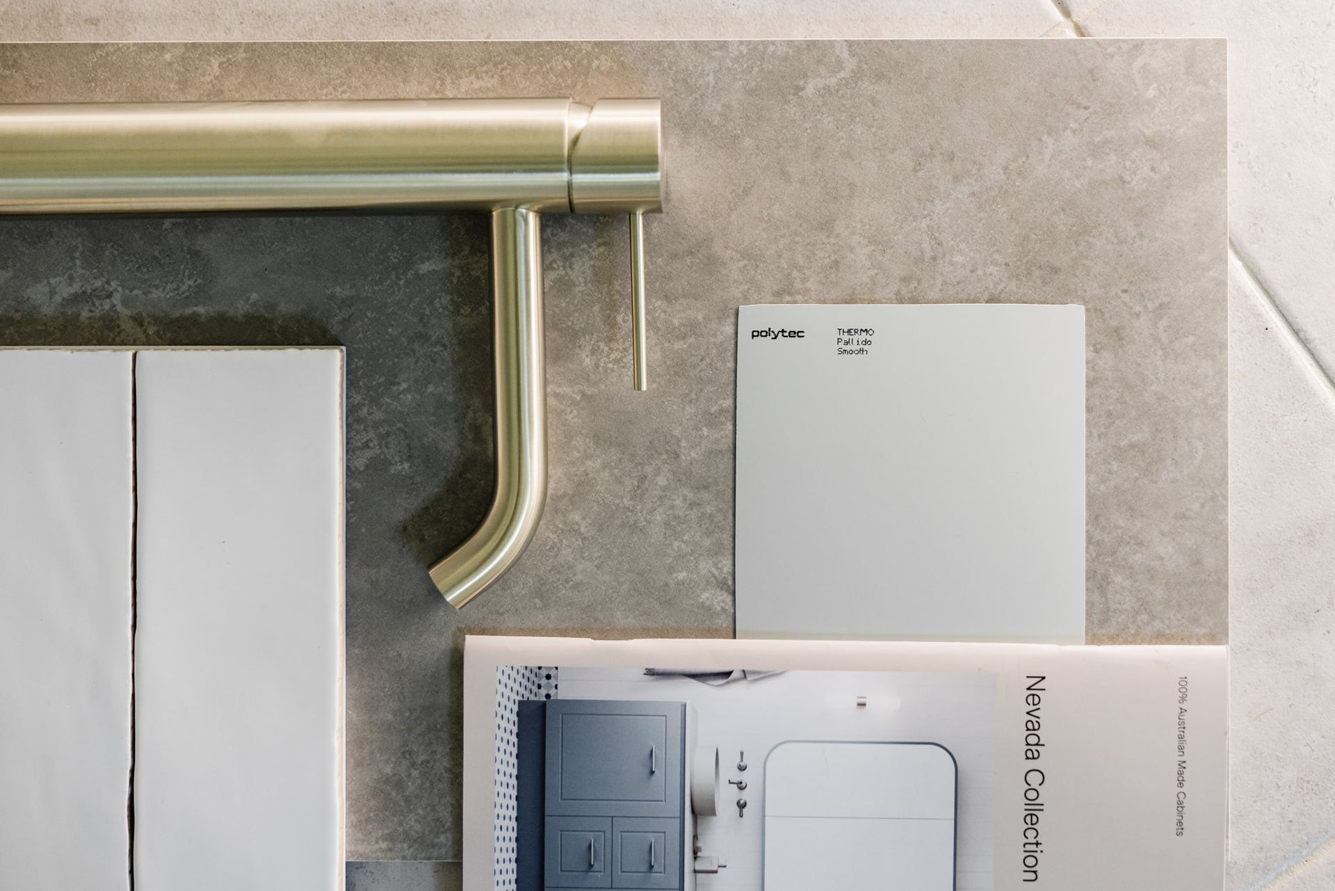 A design layout with brass faucet, gray tiles, paint swatch, and magazine.