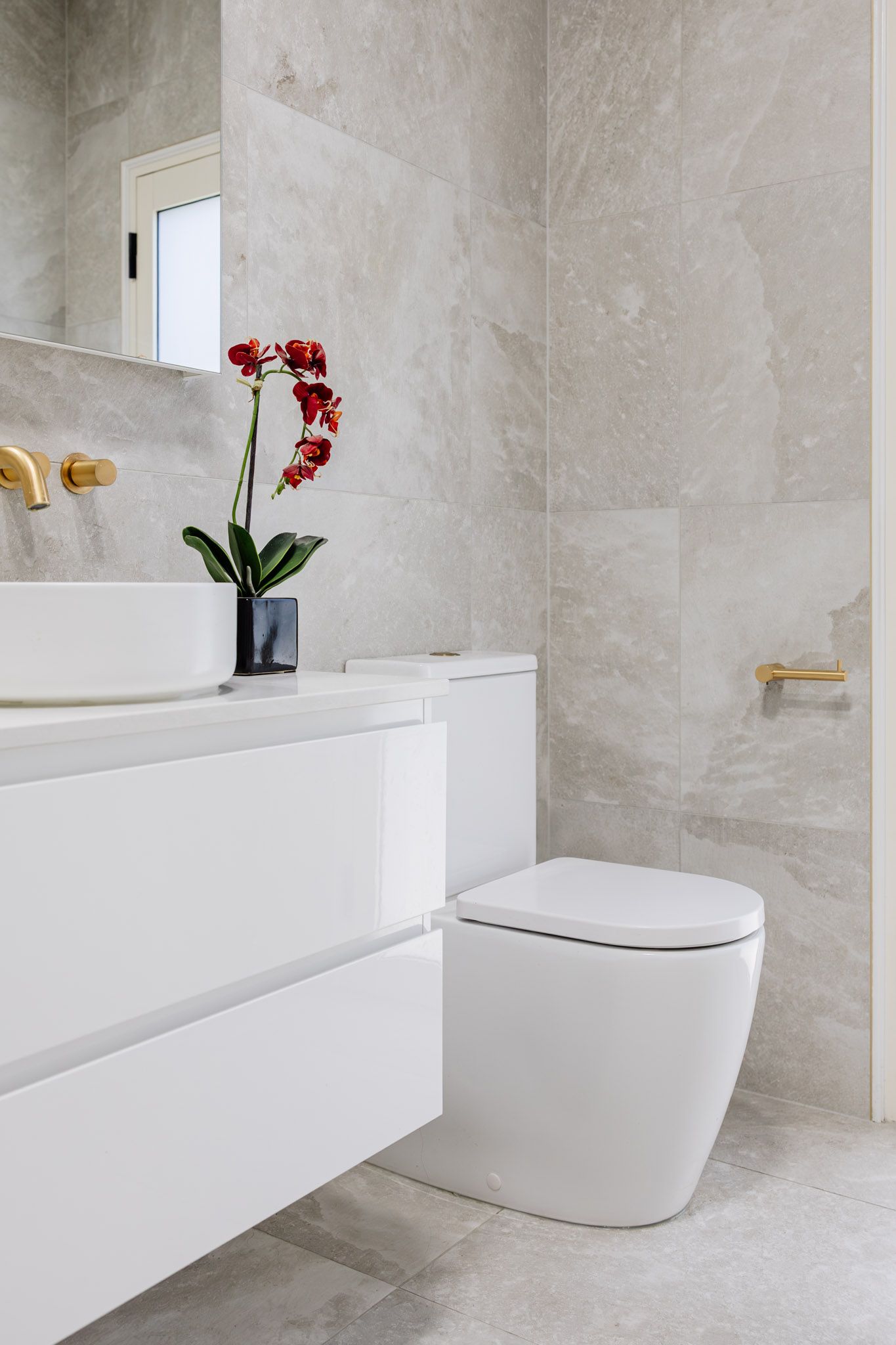 Modern white bathroom with grey tiled wall, white vanity, and a red flower.