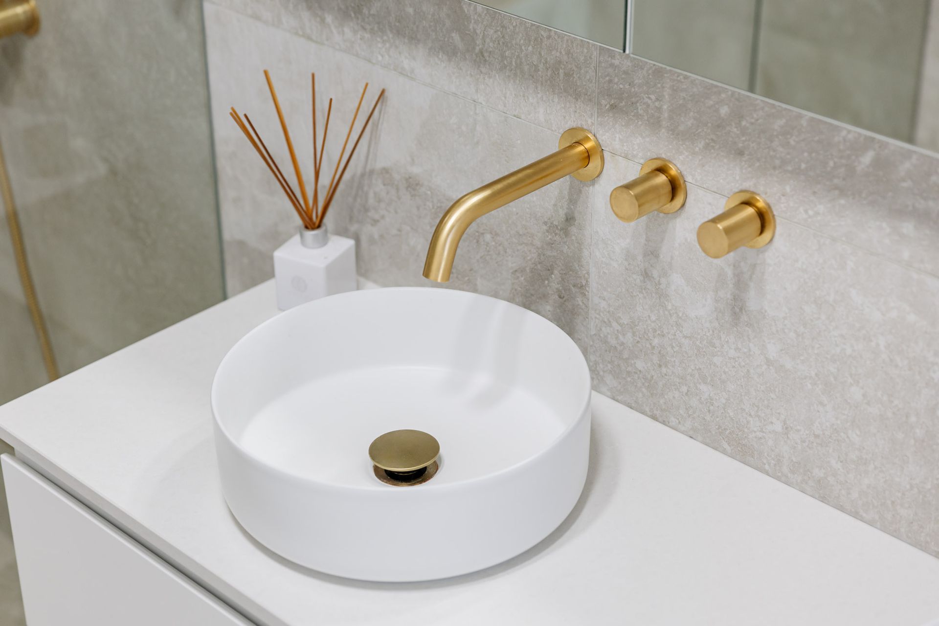 White vessel sink with gold faucet and hardware on a white countertop.