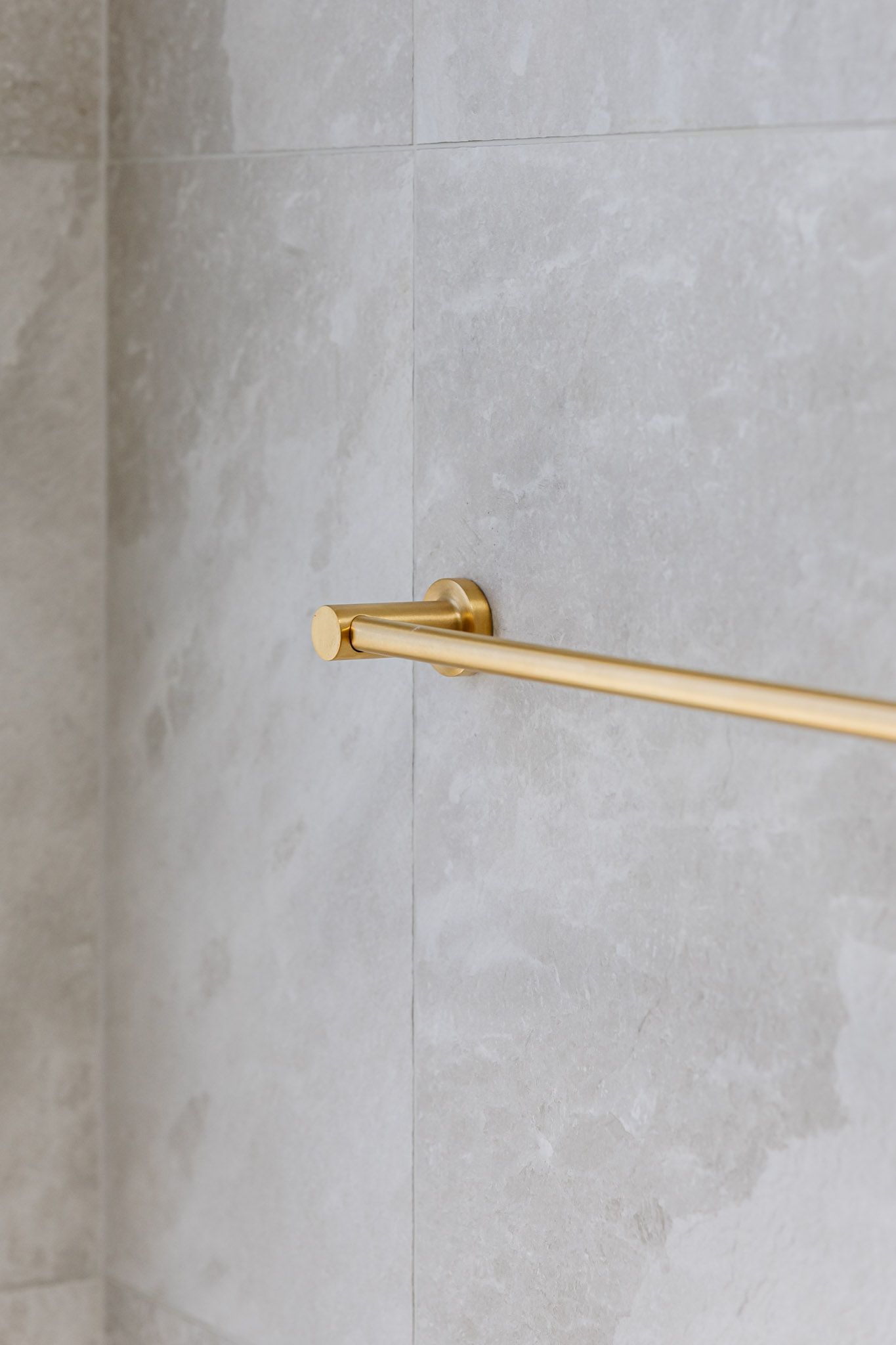 Gold towel bar mounted on light gray tiled wall.