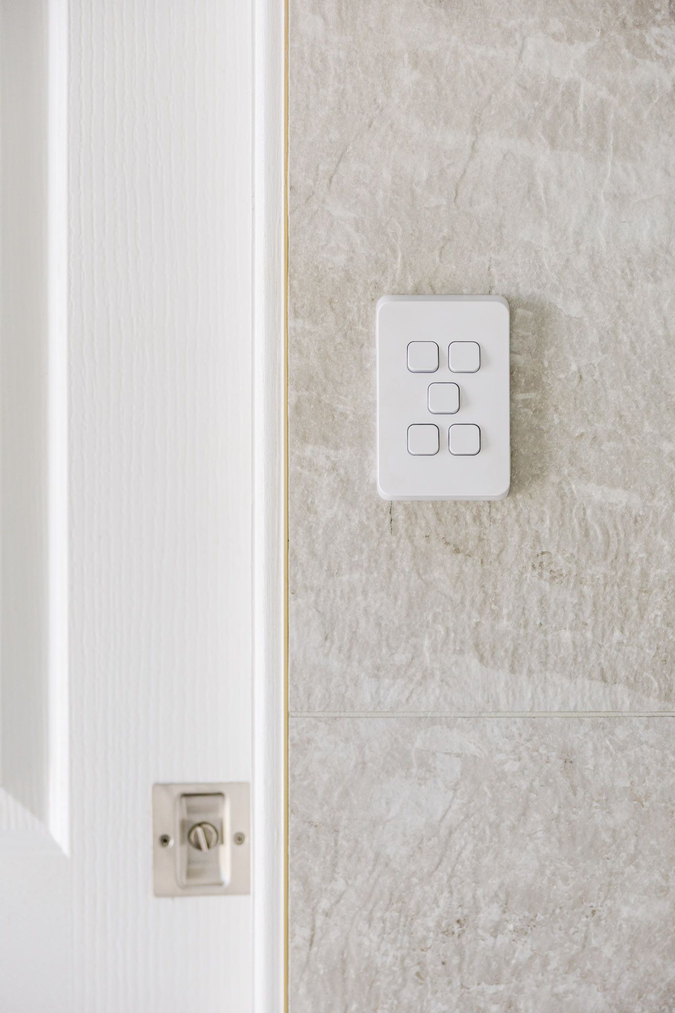 White door with a light switch on a textured gray wall. A small lock is also visible on the door.