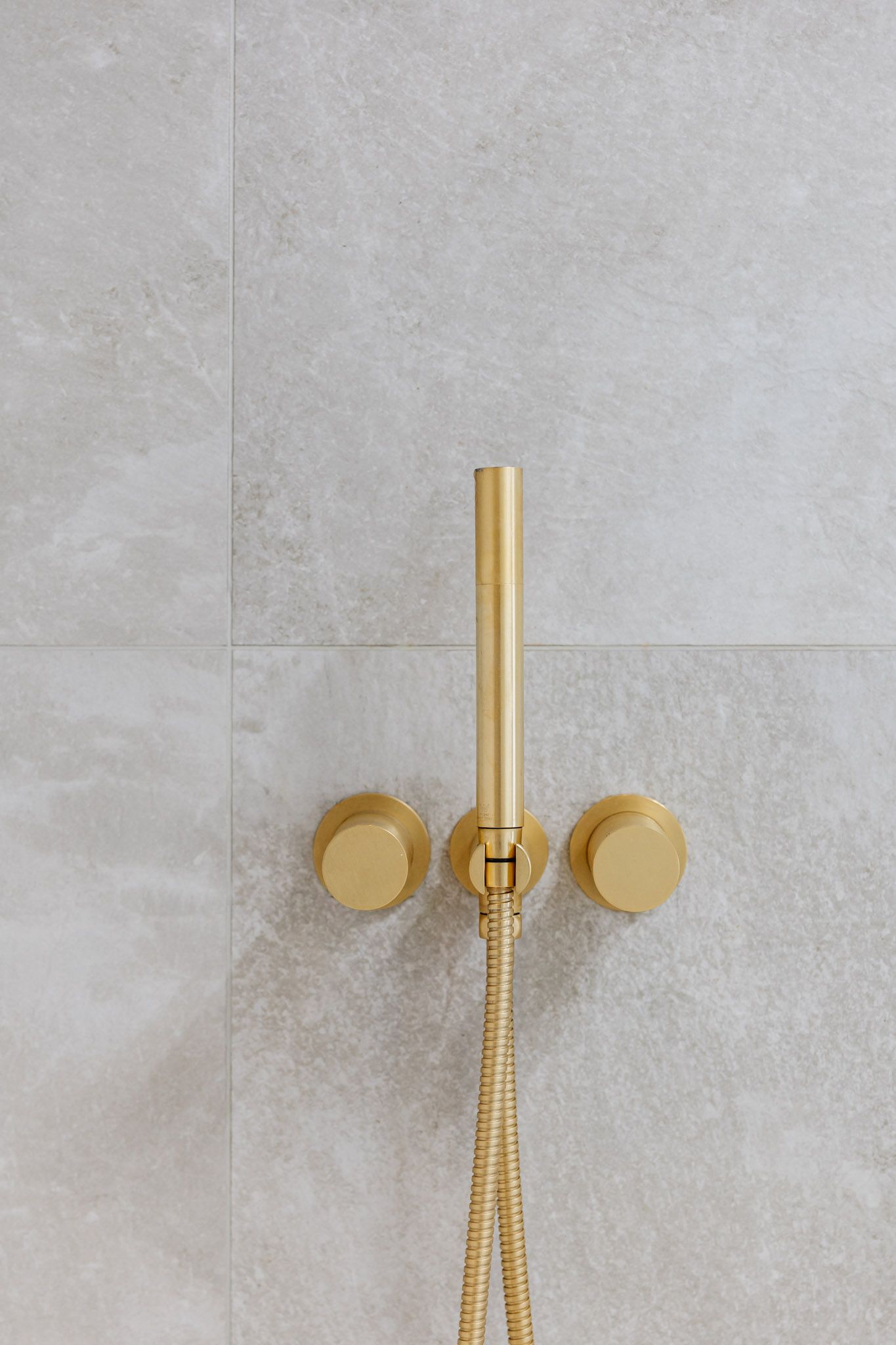 Gold shower fixtures on a light gray tiled wall.