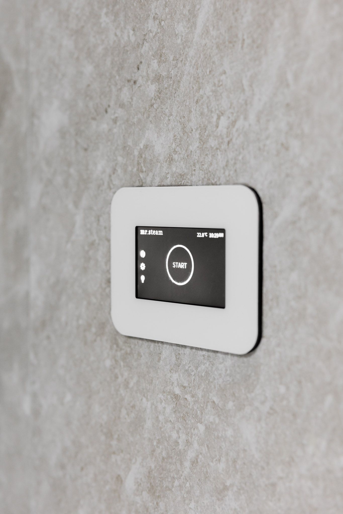 White-framed thermostat on a stone-textured wall, display showing temperature and other data.