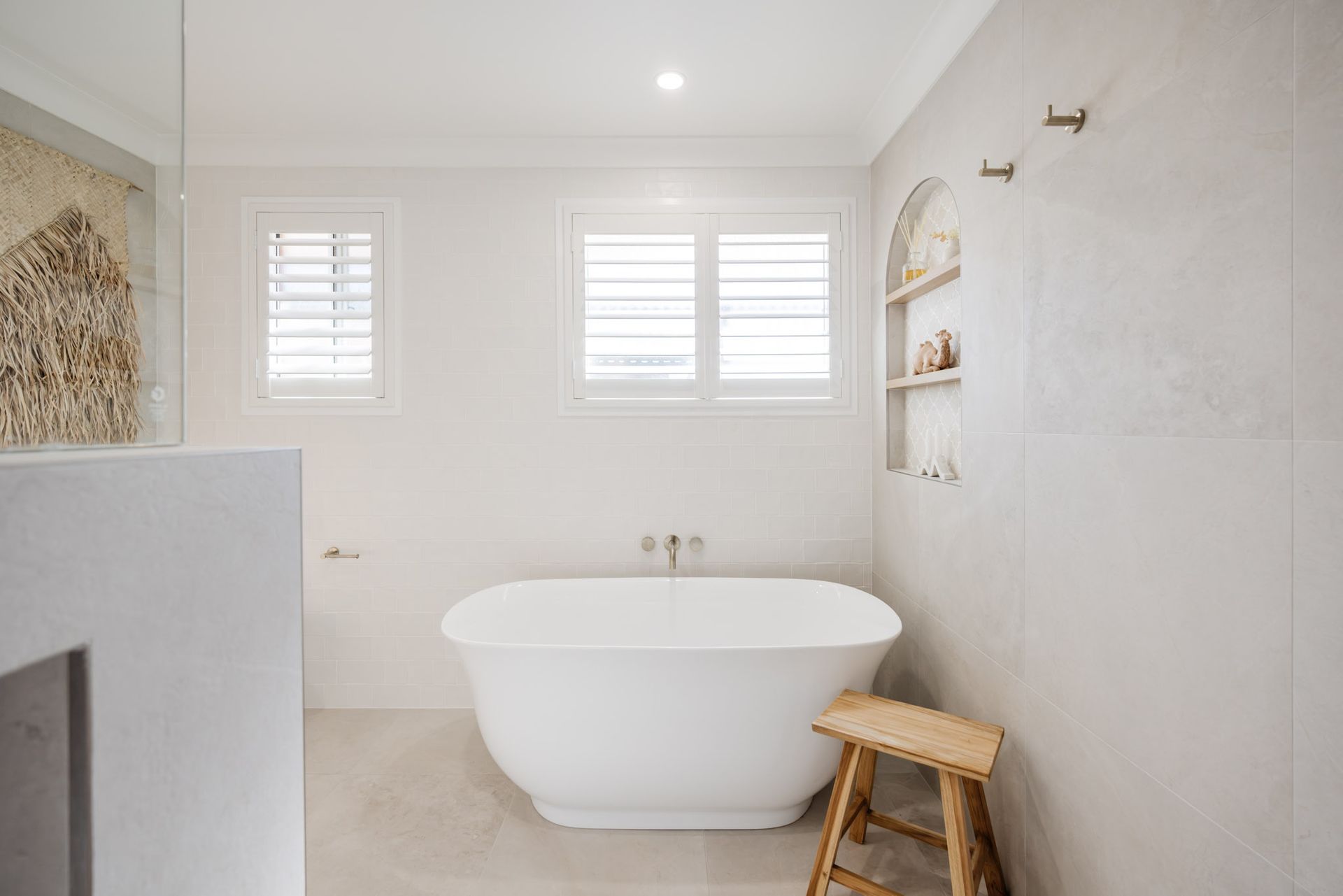 White bathroom with a freestanding tub, shutters, and a wooden stool.