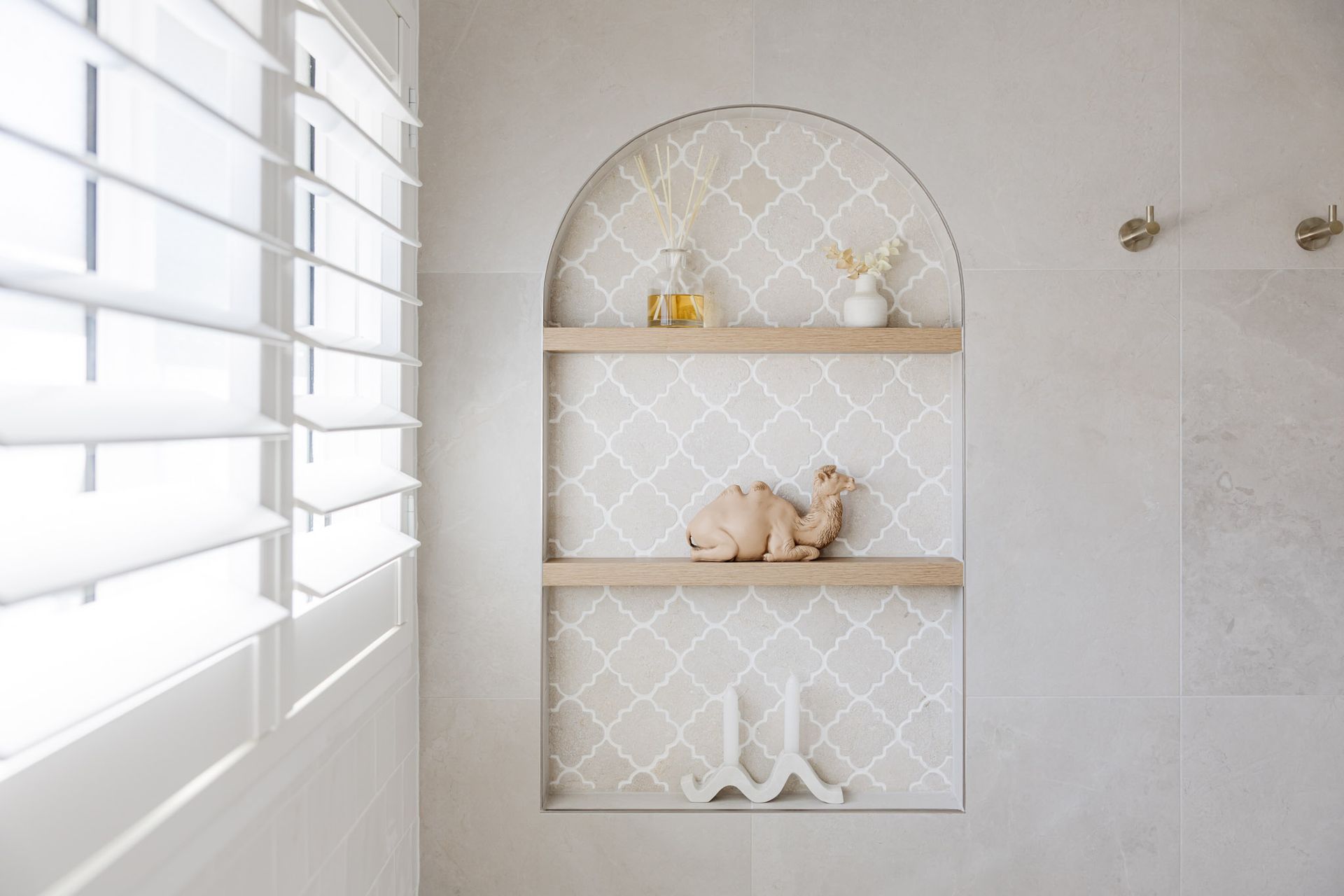 Built-in arched wall shelf with decorative items: camel figurine, vases, and candles in a modern, neutral-toned bathroom.