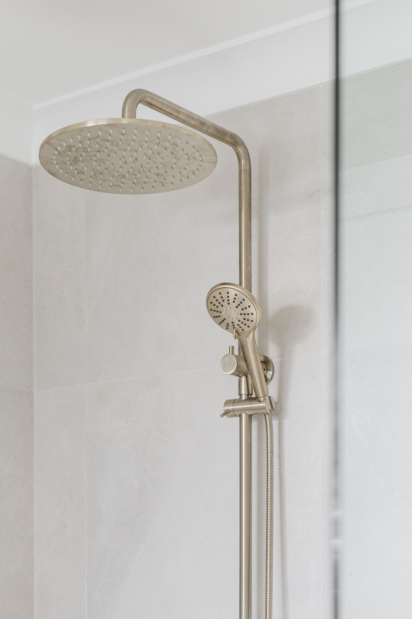 Silver shower head and handheld sprayer on a white tiled wall, inside a shower.