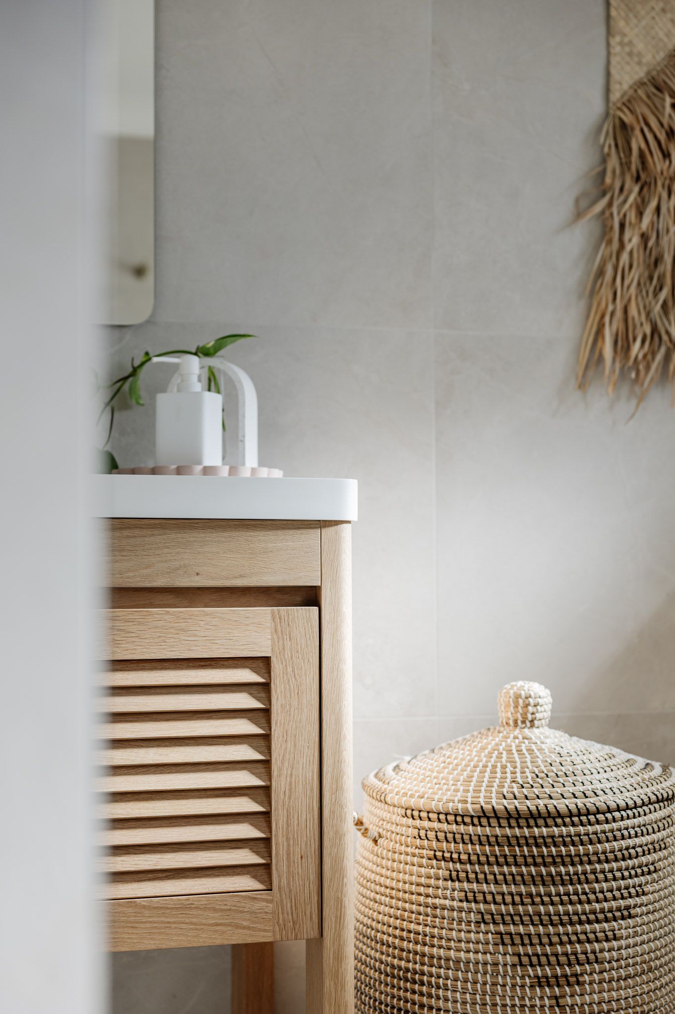 Wooden bathroom vanity with a louvered door, a woven basket, and decorative elements.