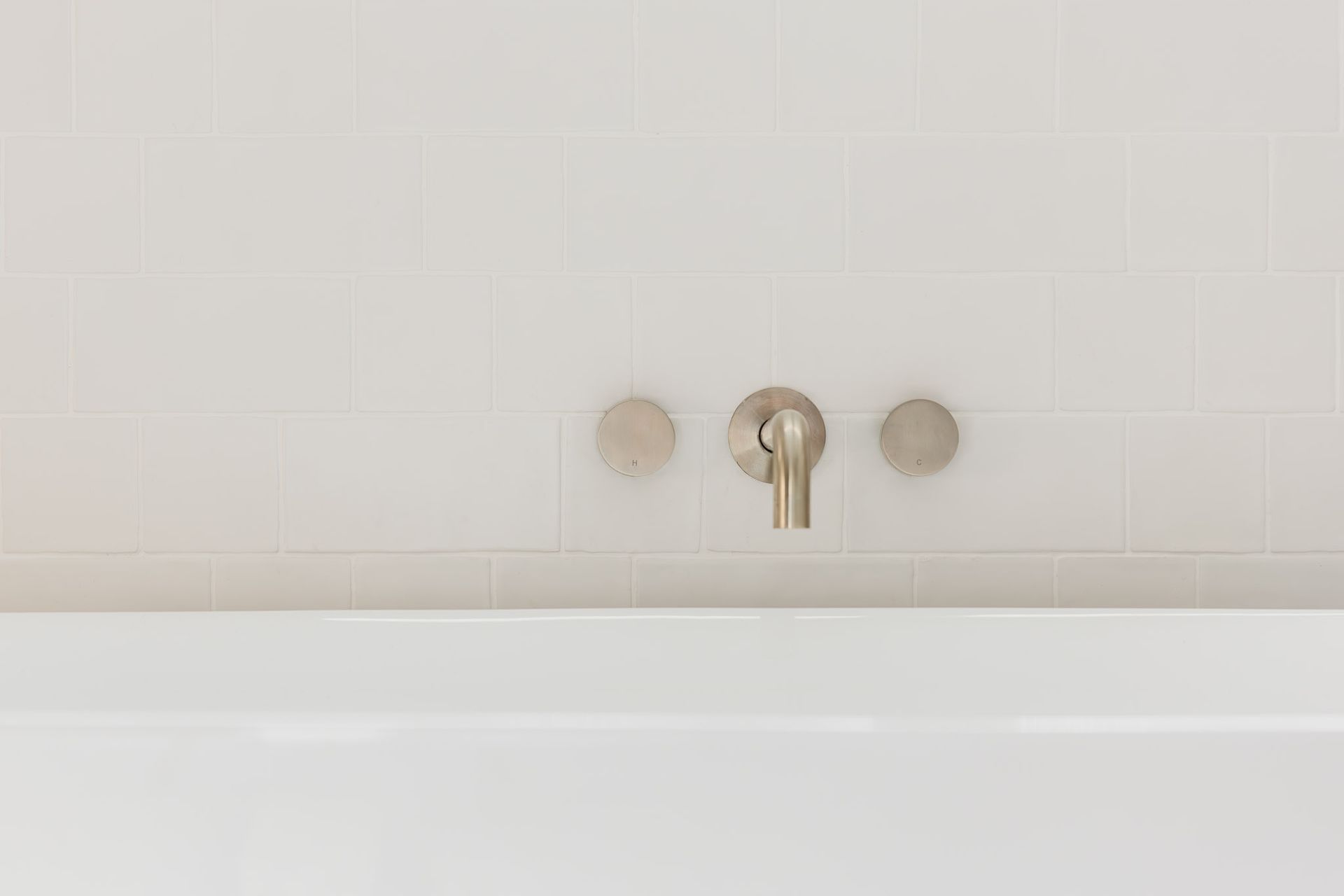 White bathtub with silver faucet and circular control knobs, set against white tiled wall.