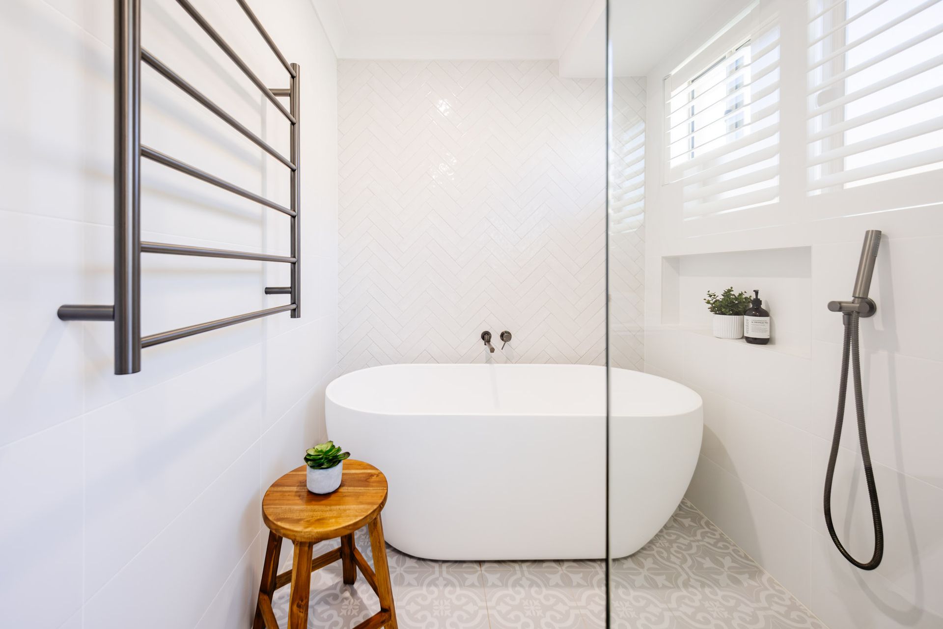 Modern white bathroom with freestanding tub, glass shower, and wooden stool.
