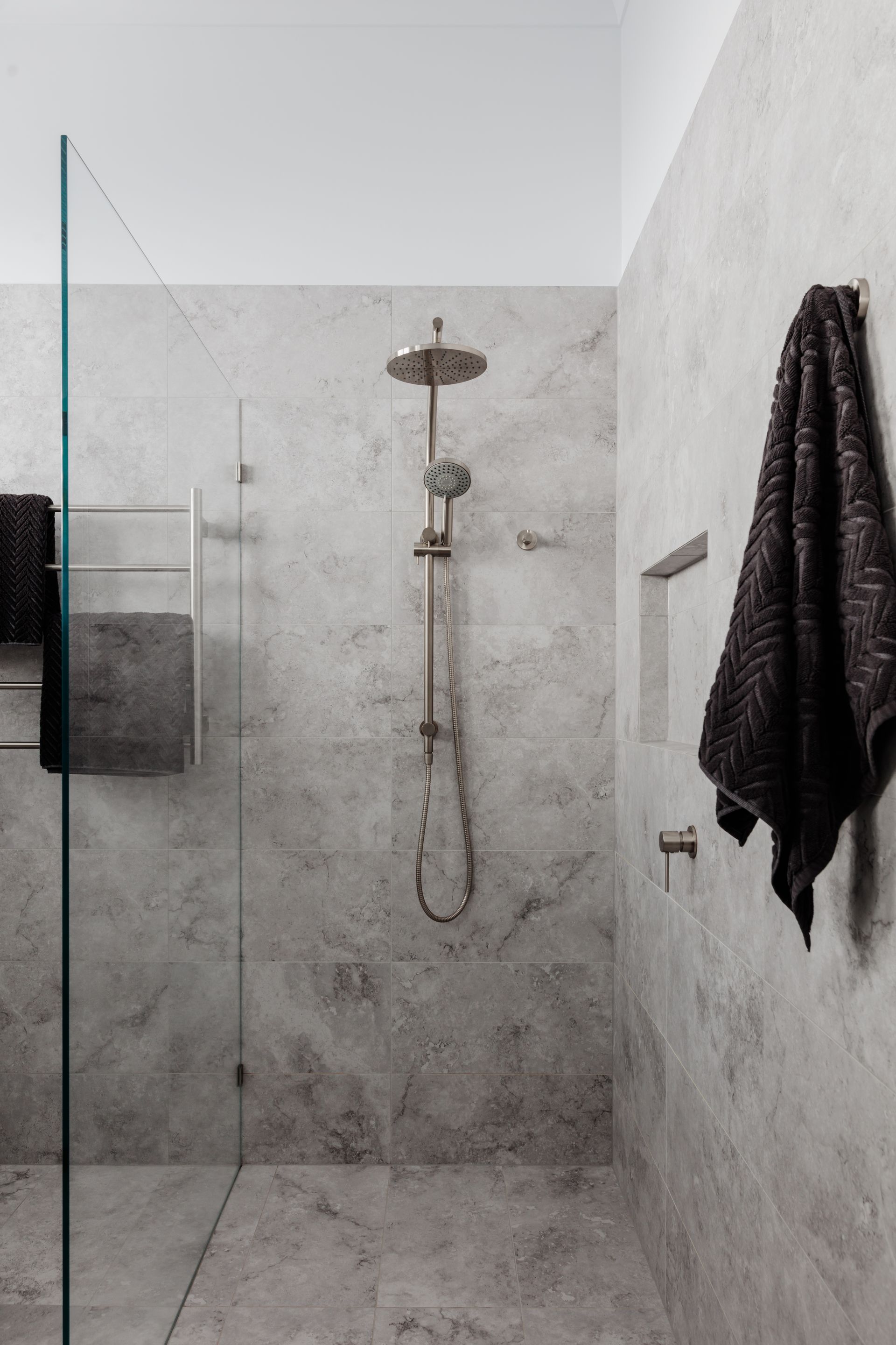 Modern gray tiled shower with glass door, towel racks, and black towels.