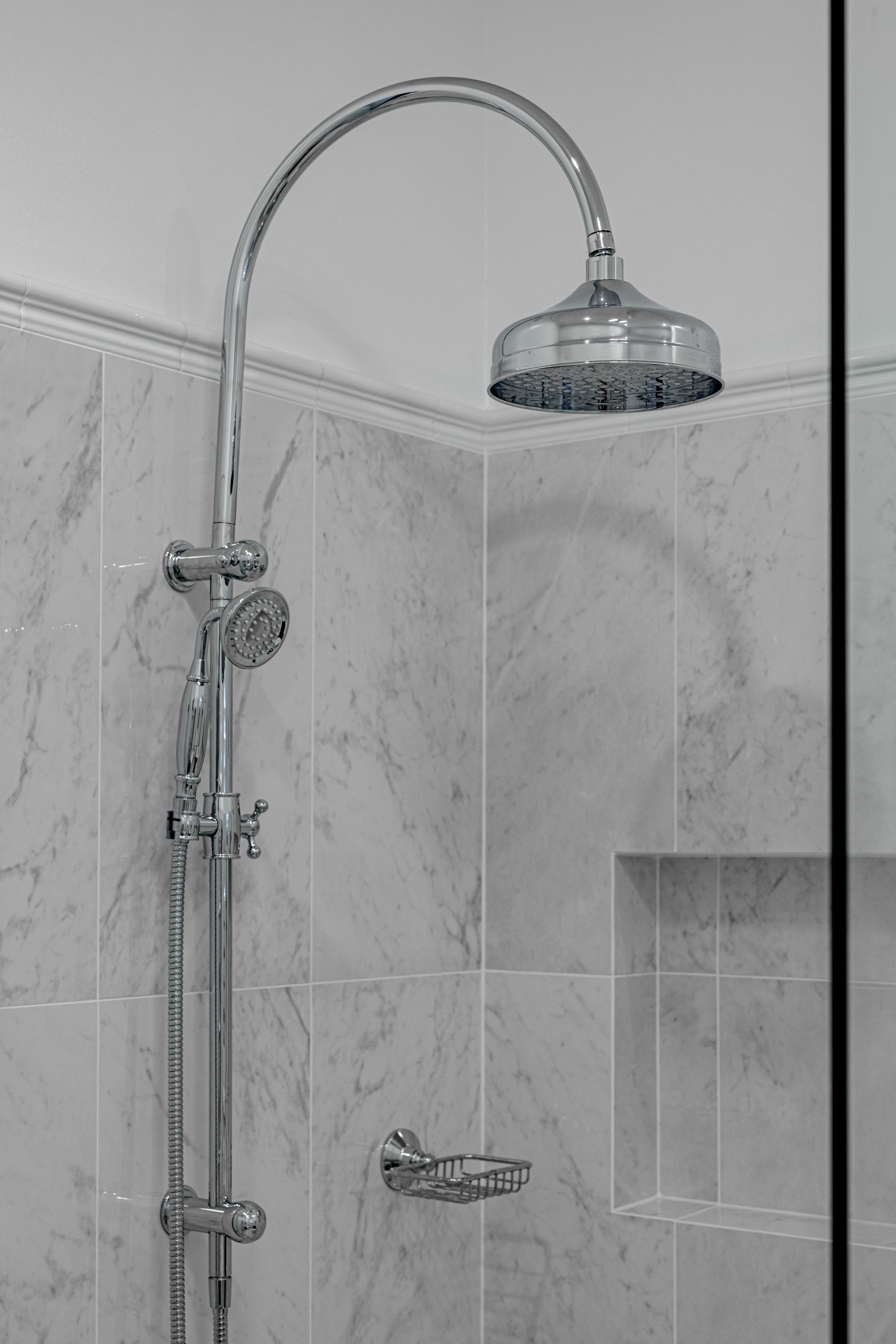 Silver shower fixture in a marble-tiled shower, with a large rain showerhead and a handheld showerhead.