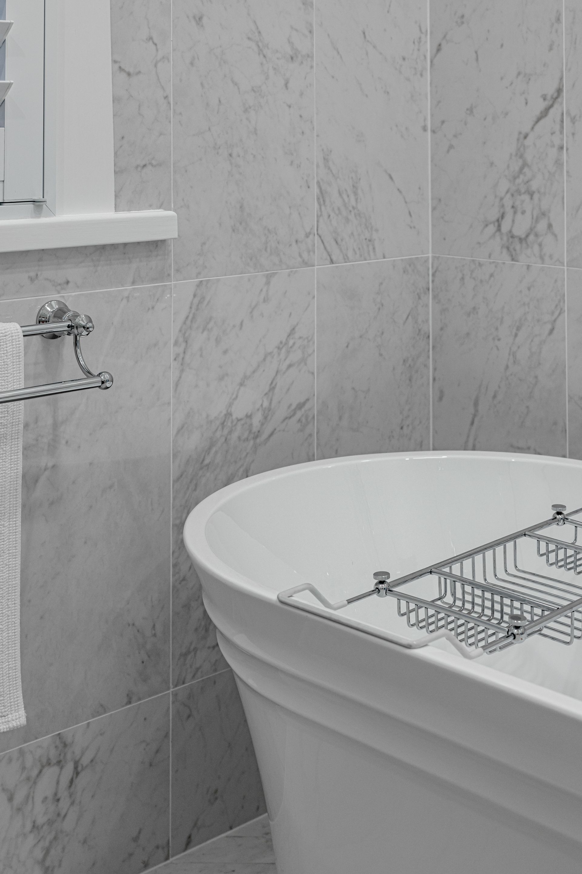 White marble bathroom with a freestanding tub and towel rack.