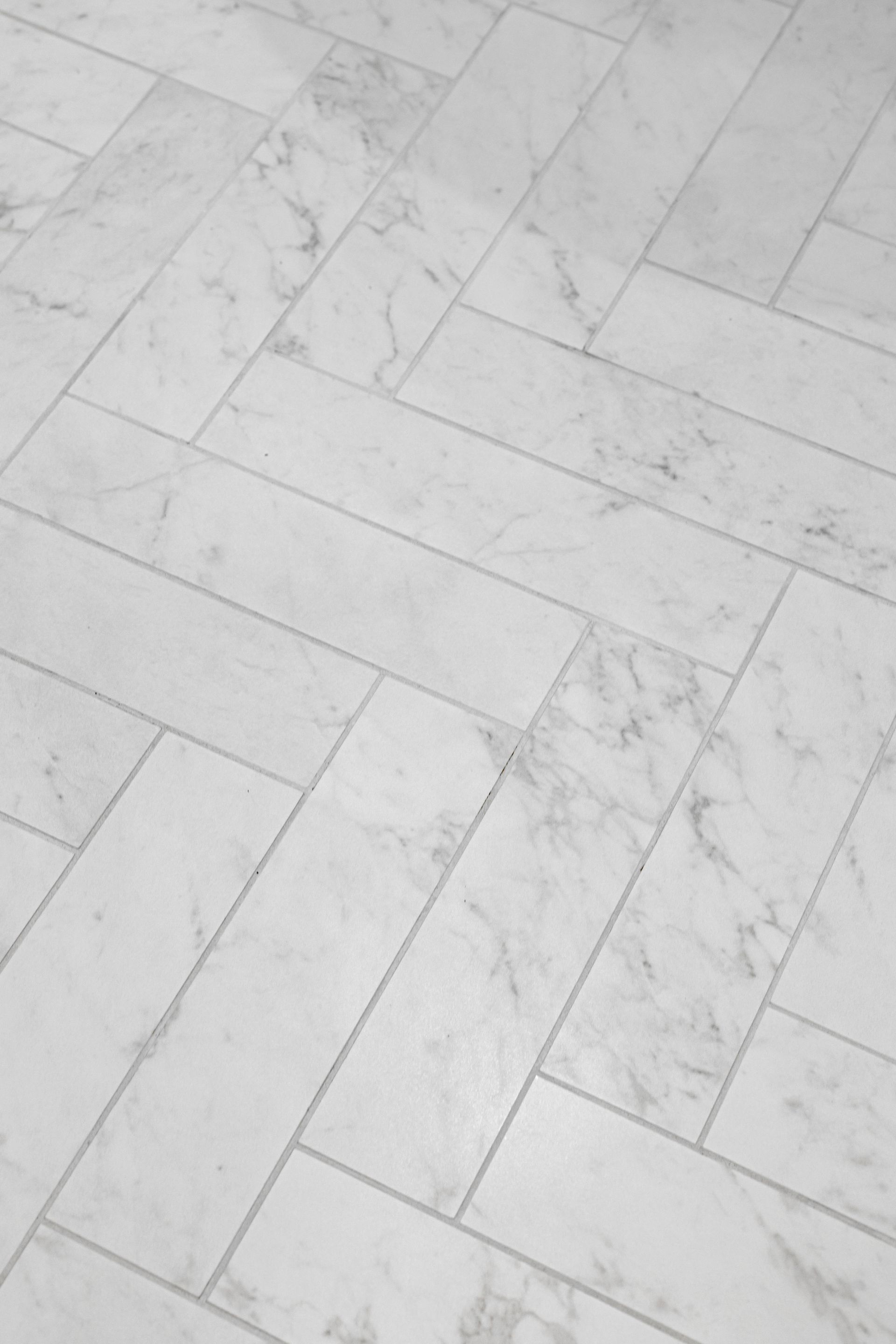 Herringbone pattern of light gray tiles, mimicking marble, on a floor.