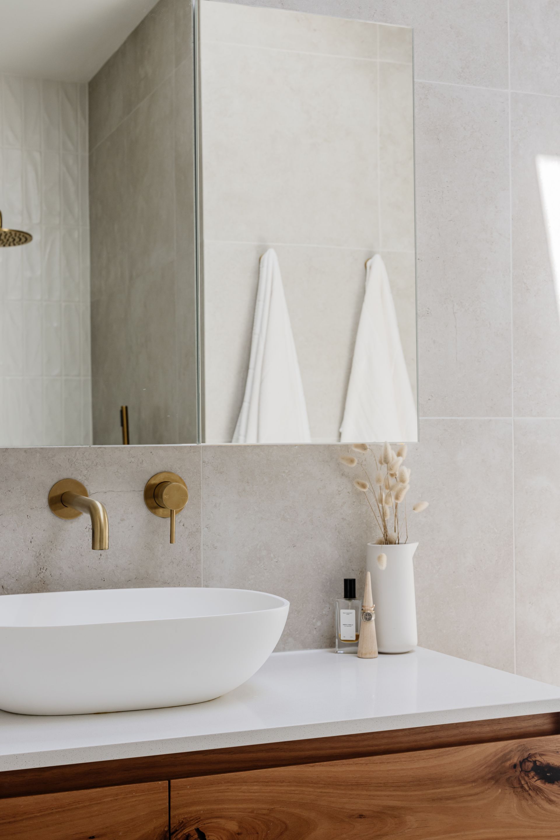 Bathroom with white vessel sink, brass faucet, and white towels hanging under a mirror.