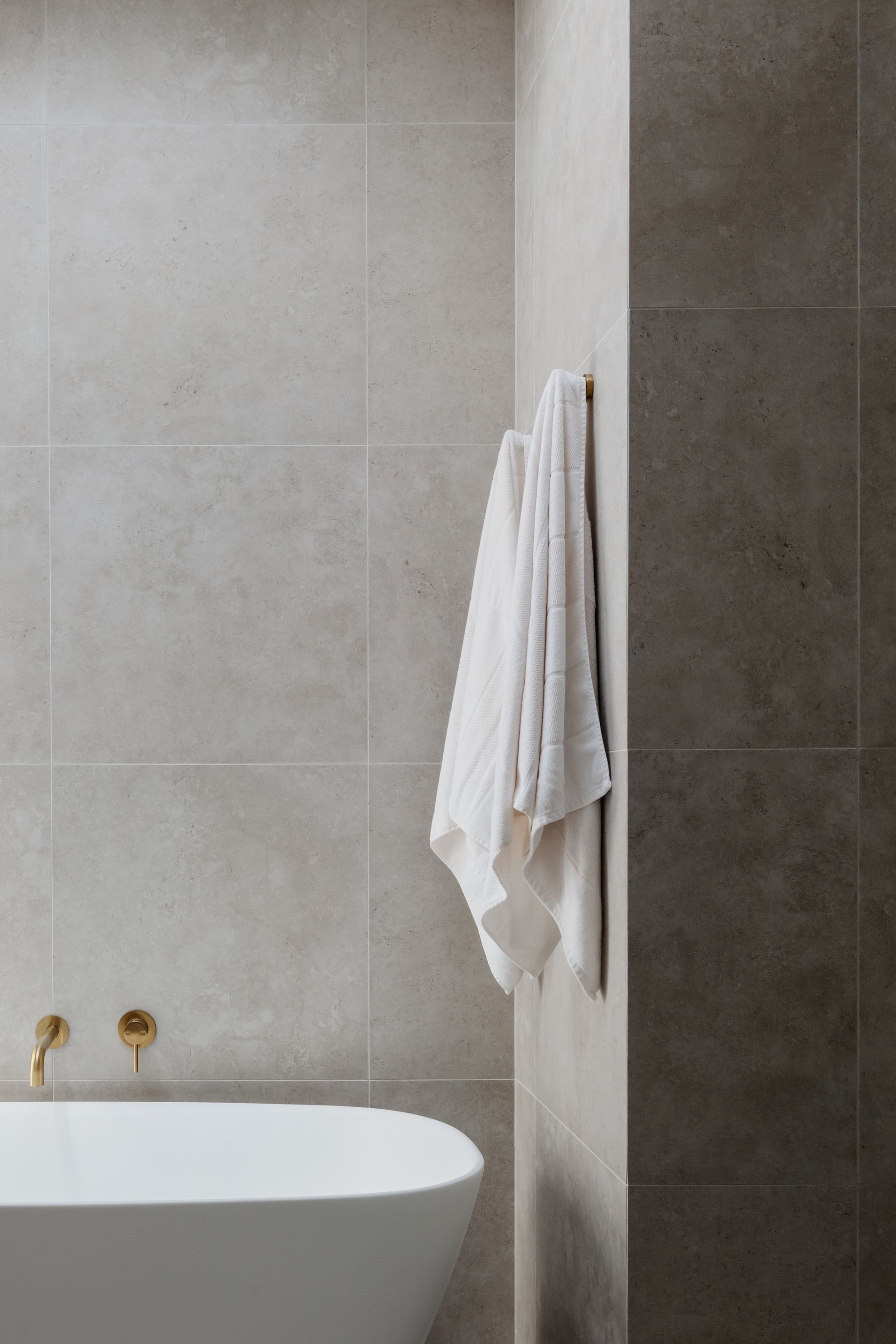 Bathroom with a white towel on a wall-mounted towel rack, next to a bathtub and grey tiled walls.