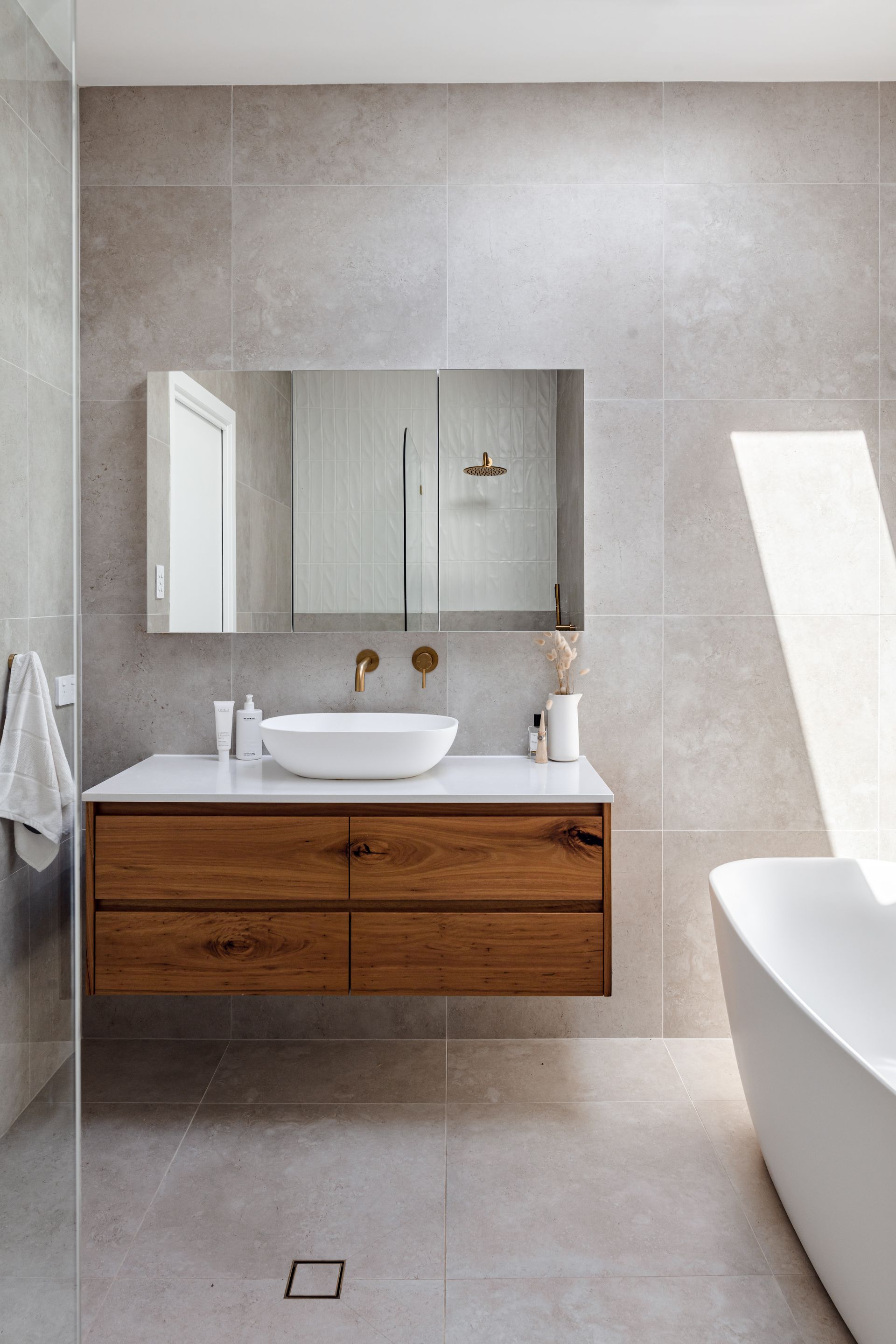 Modern bathroom with a floating wooden vanity, white sink, large mirror, and freestanding tub.