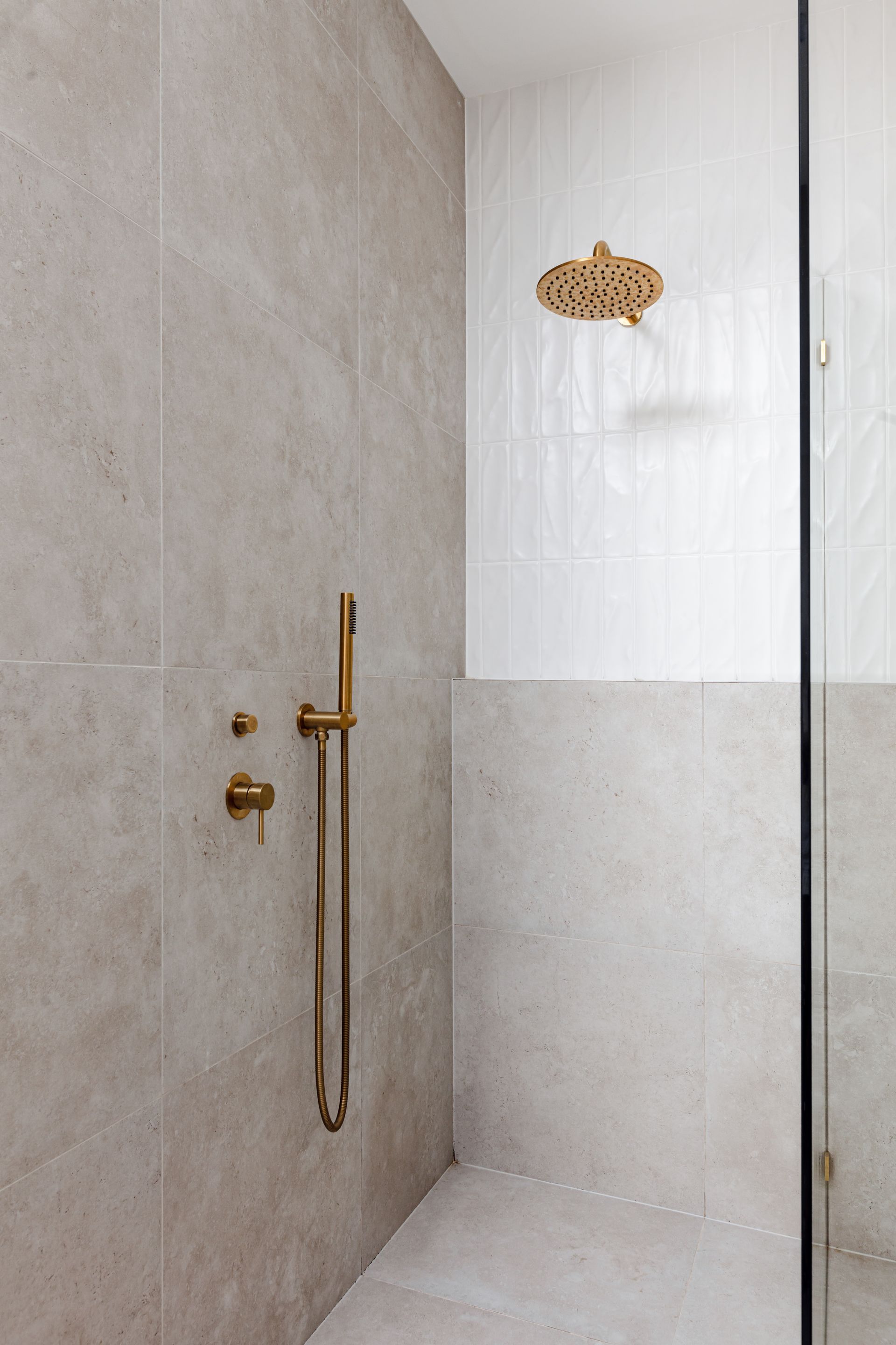 Shower with beige tile walls and gold fixtures.