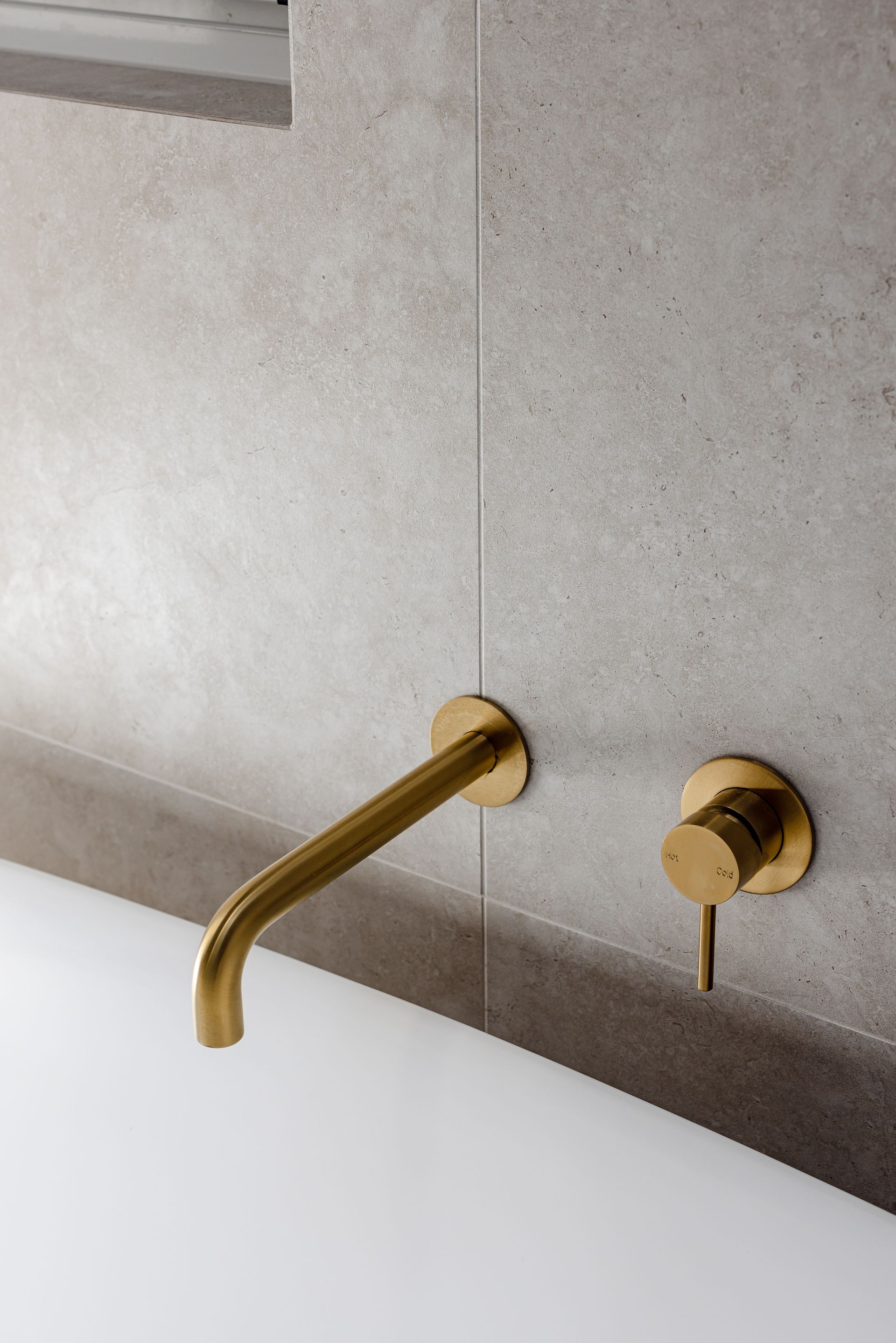 Gold faucet and lever on a light gray tiled wall.