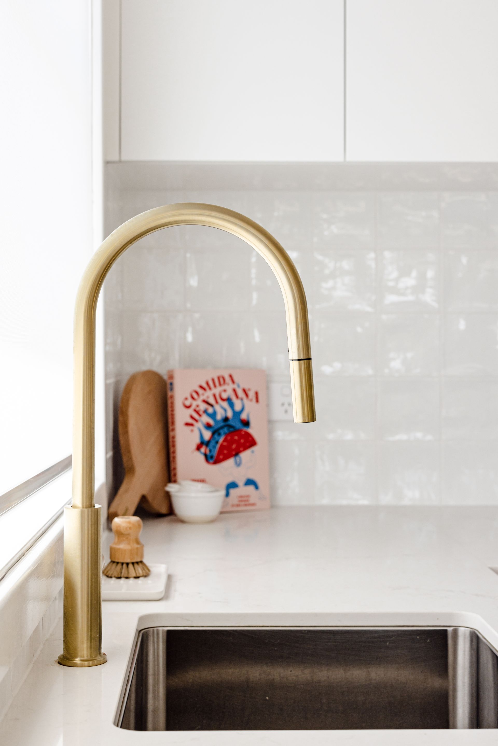 Gold kitchen faucet over a stainless steel sink, with white countertop and backsplash.