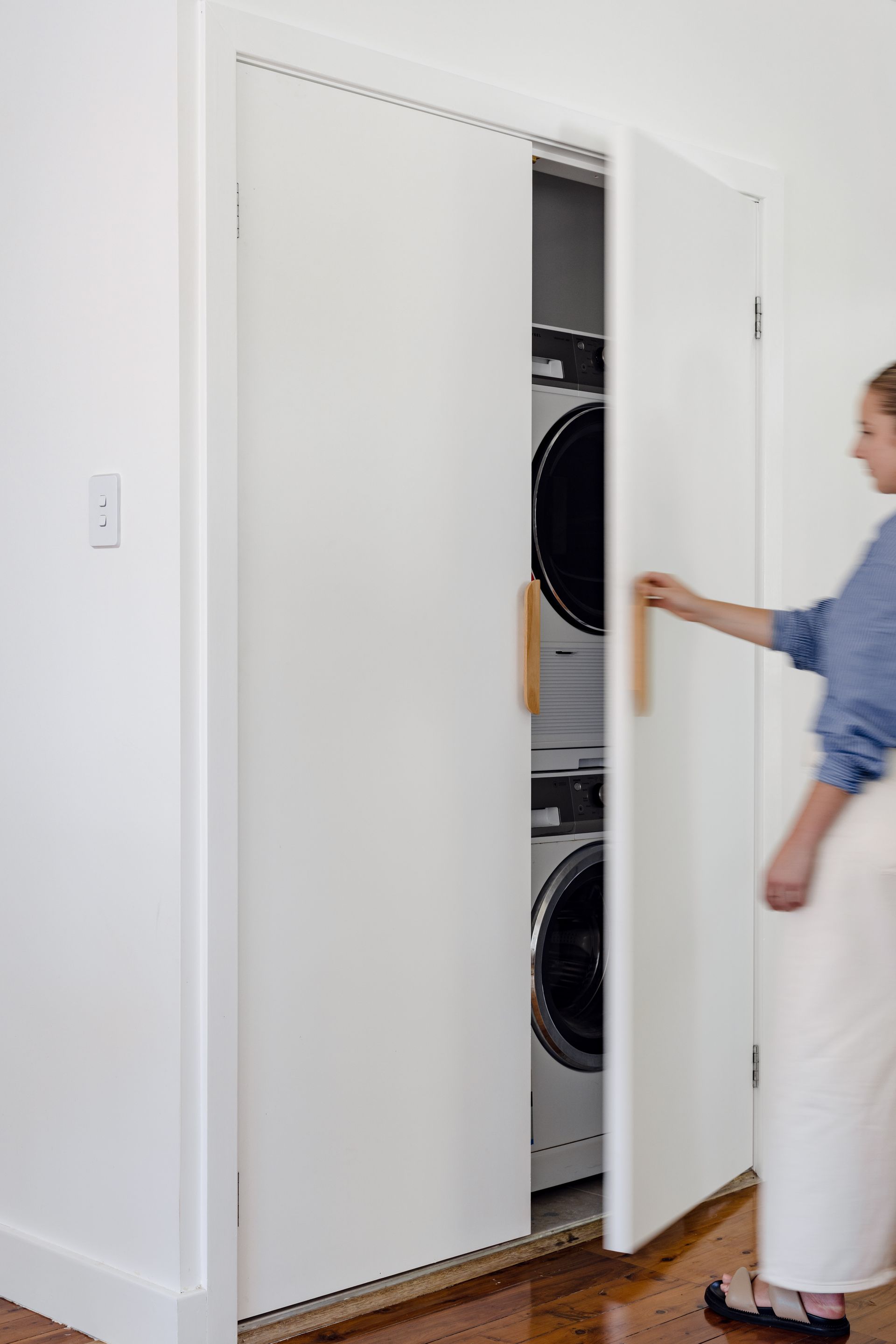 Woman opening a white closet door revealing a stacked washer and dryer.